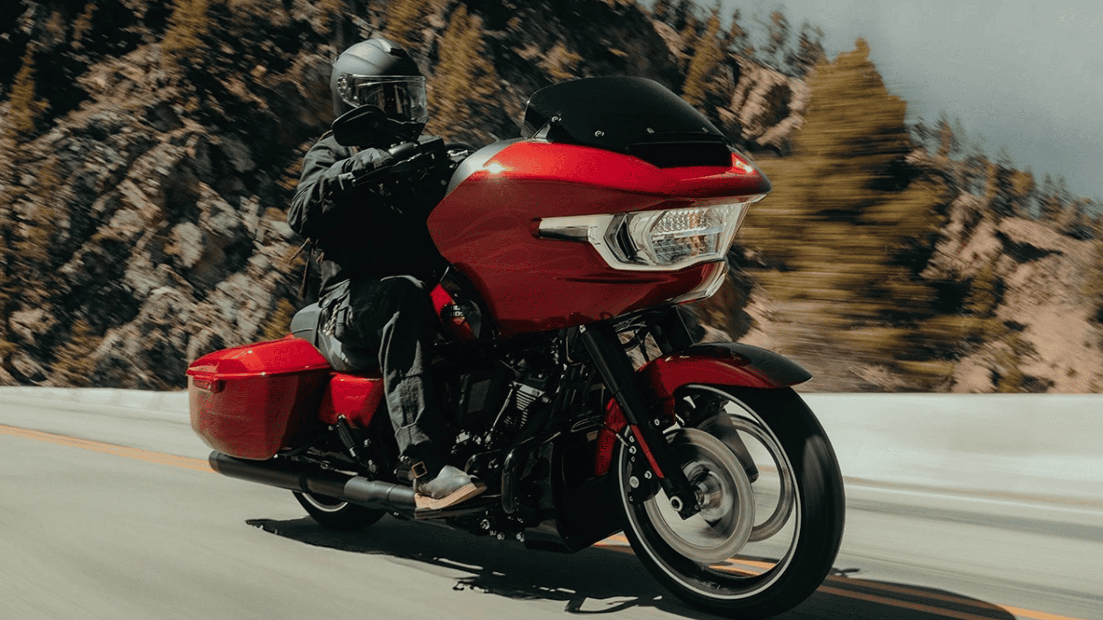A rider cruising on a striking red 2025 Harley-Davidson® Road Glide® along a scenic mountain road