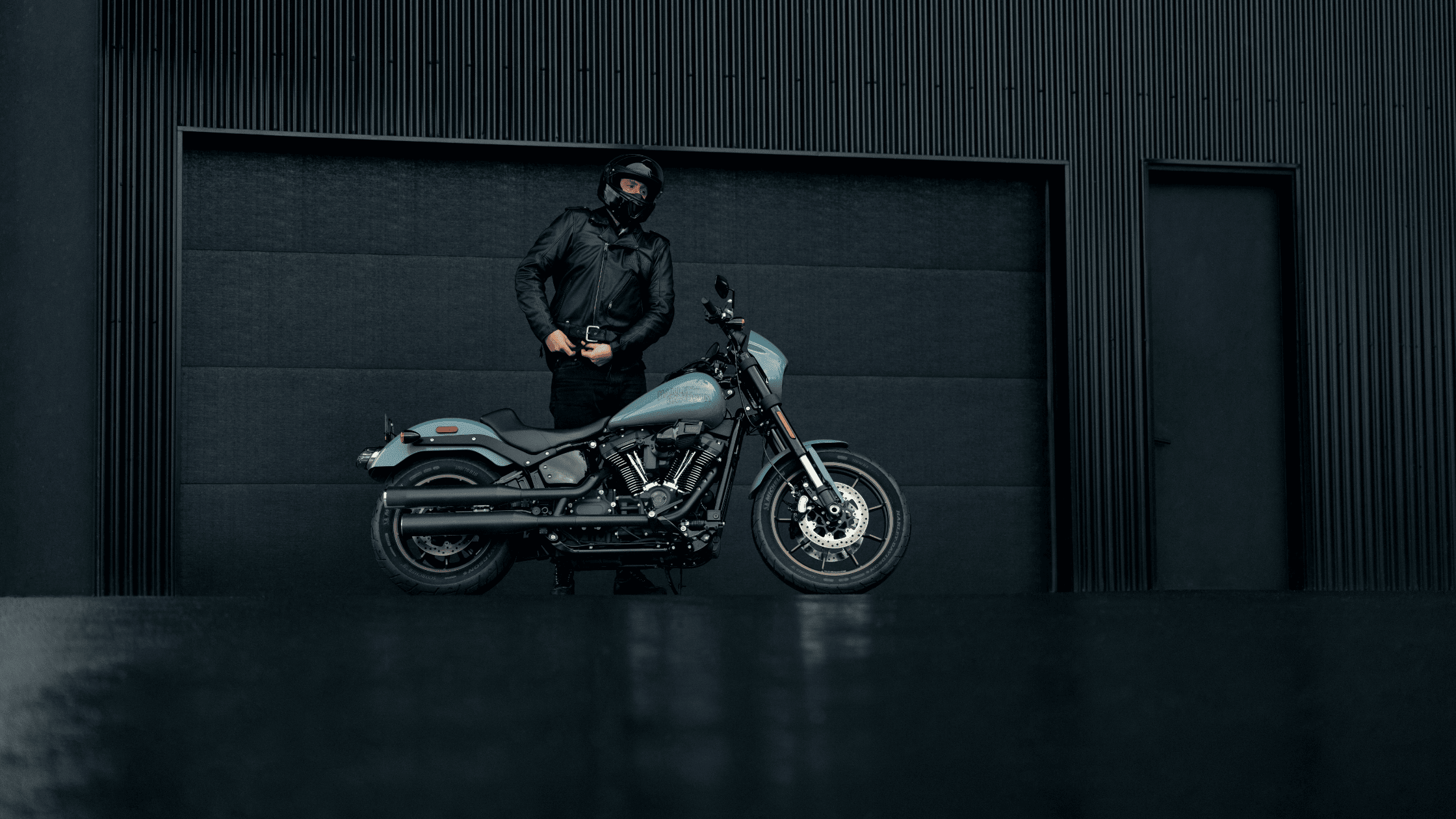 A rider standing beside a 2024 Harley-Davidson® Low Rider® S against a sleek, dark industrial backdrop