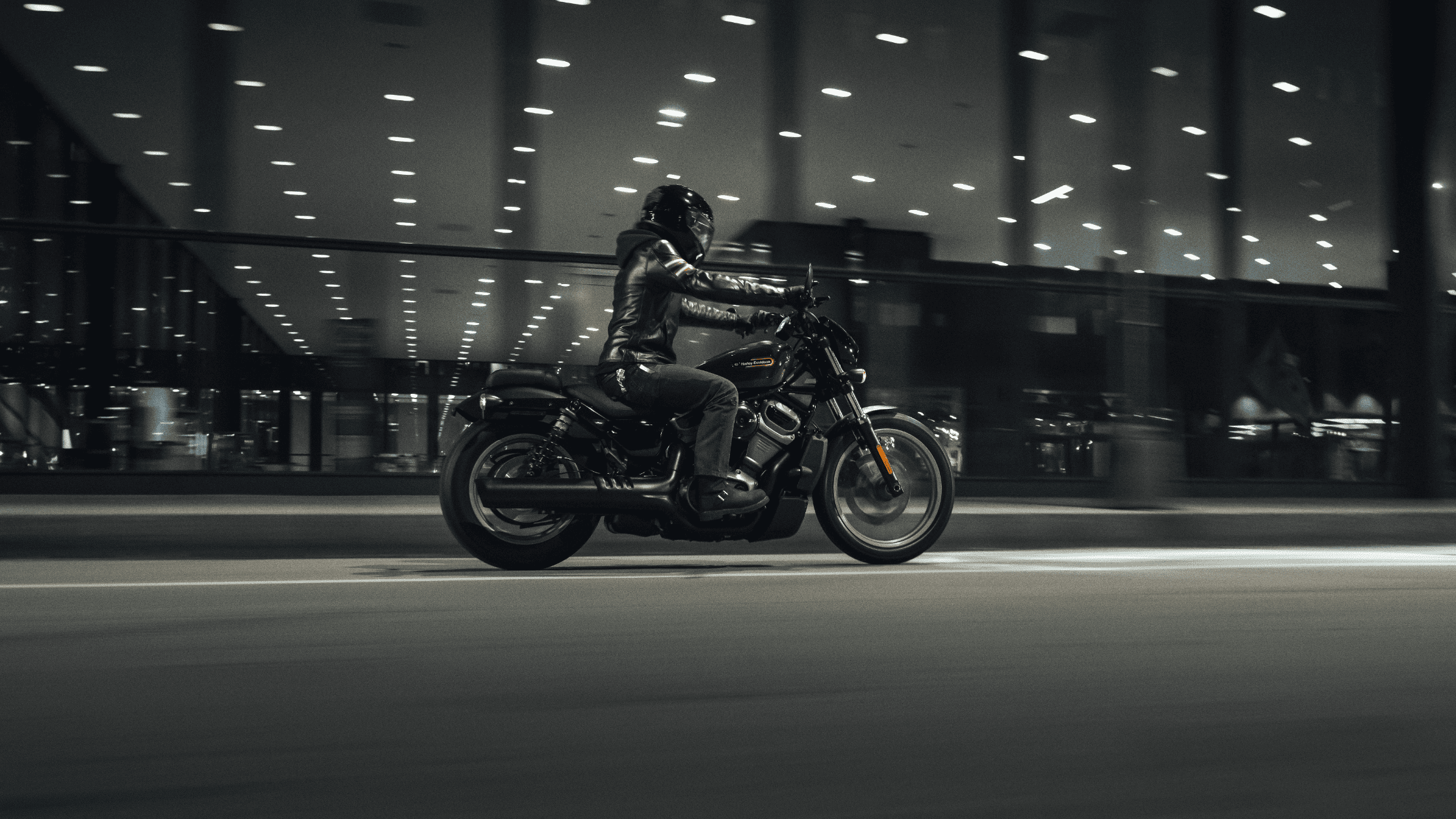 A rider on a black 2024 Harley-Davidson® Nightster® Special cruising the streets and a building on the background.