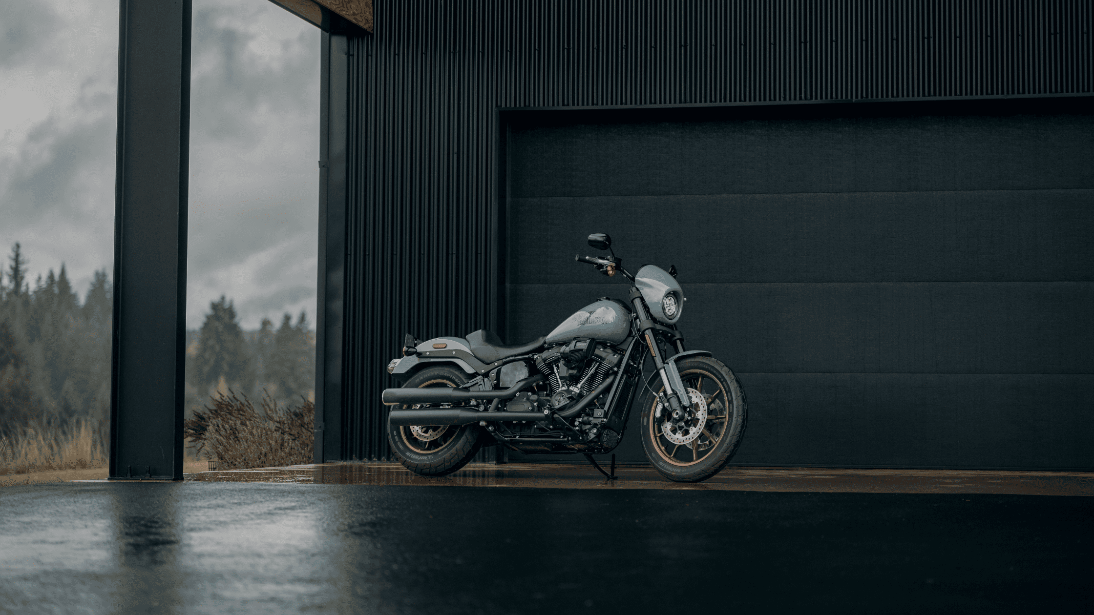 A 2024 Harley-Davidson® Low Rider® S parked against a modern black industrial backdrop on a rainy day
