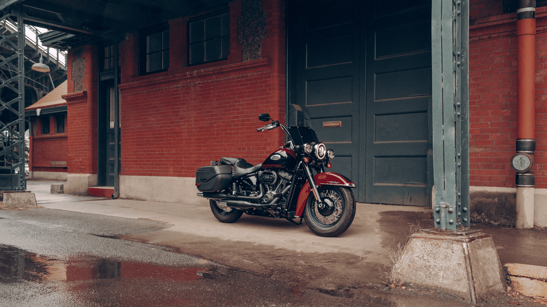 A 2024 Harley-Davidson® Heritage Classic 114 parked beside a vintage brick building on a rainy day