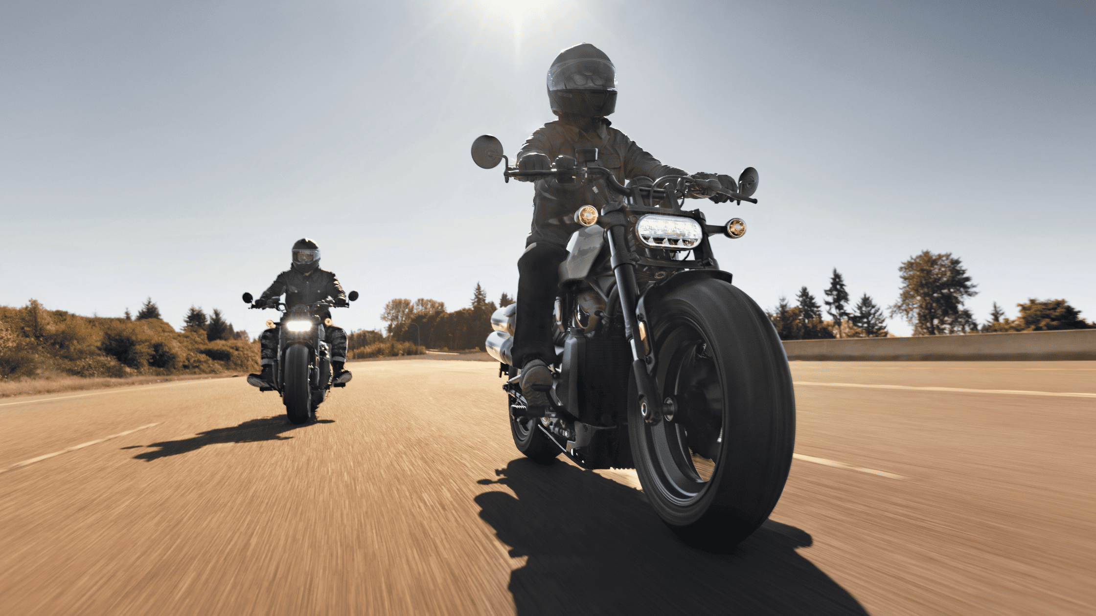 Two riders on powerful motorcycles cruising under a sunny sky on an open road.