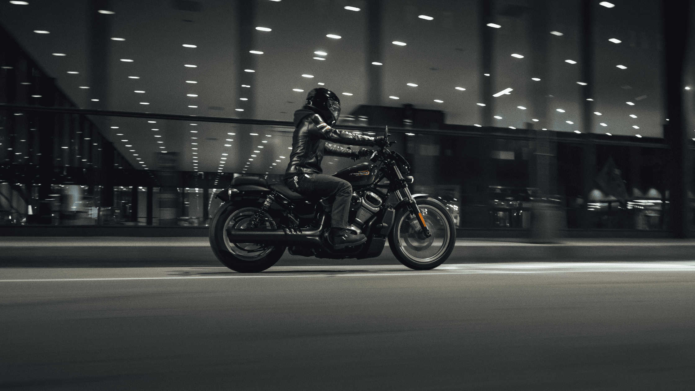 Rider on a sleek black motorcycle cruising through a city at night, lights glowing.