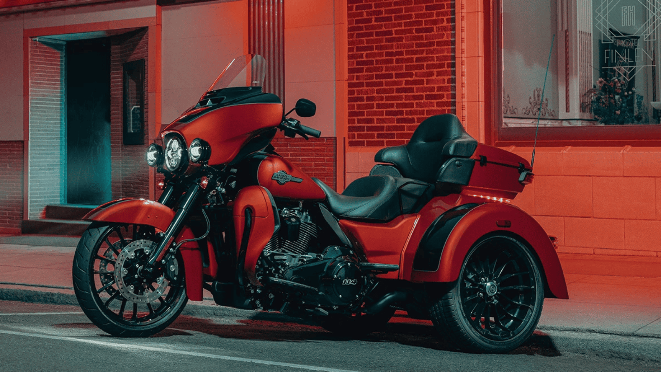 Bright red trike motorcycle parked on a street at night, illuminated by neon lights.