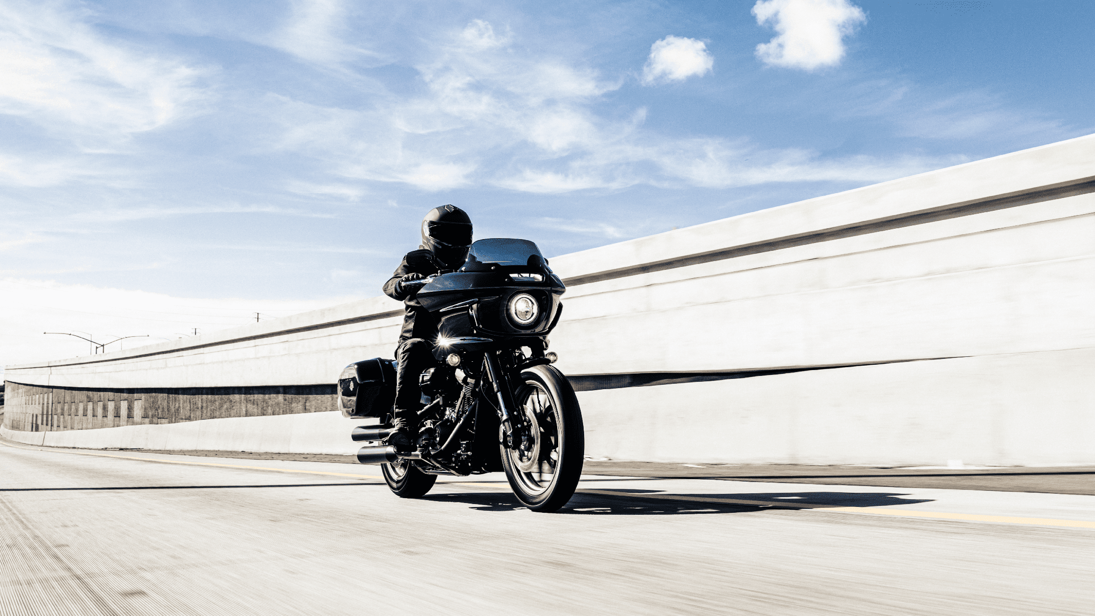 Rider on a black motorcycle cruising along a bright highway under a clear sky.