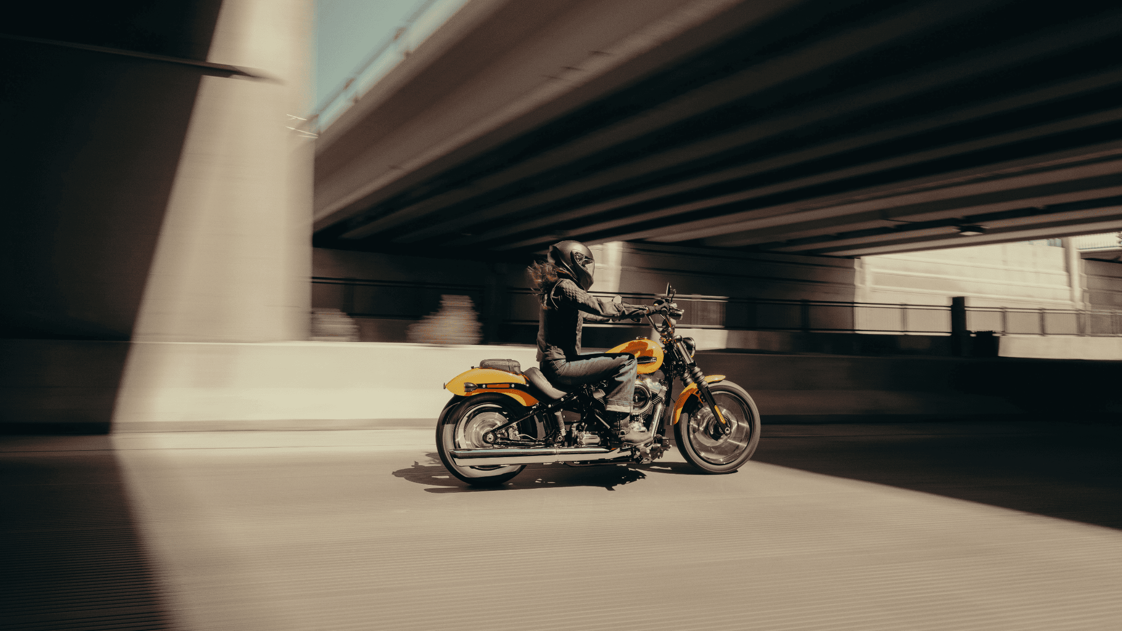 Rider on a yellow cruiser motorcycle speeding under a bridge.