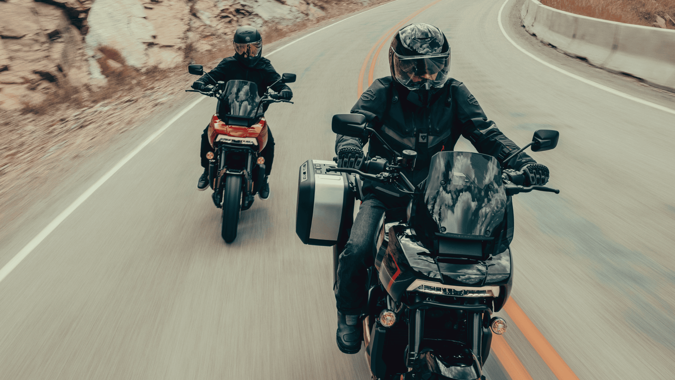 Two adventure motorcyclists riding on a winding mountain road.