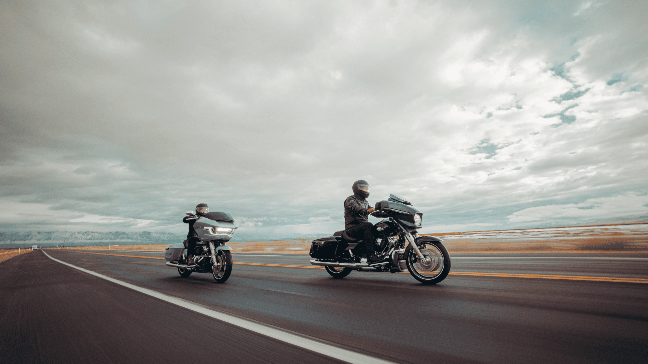Two touring motorcyclists cruising on an open highway under clouds.
