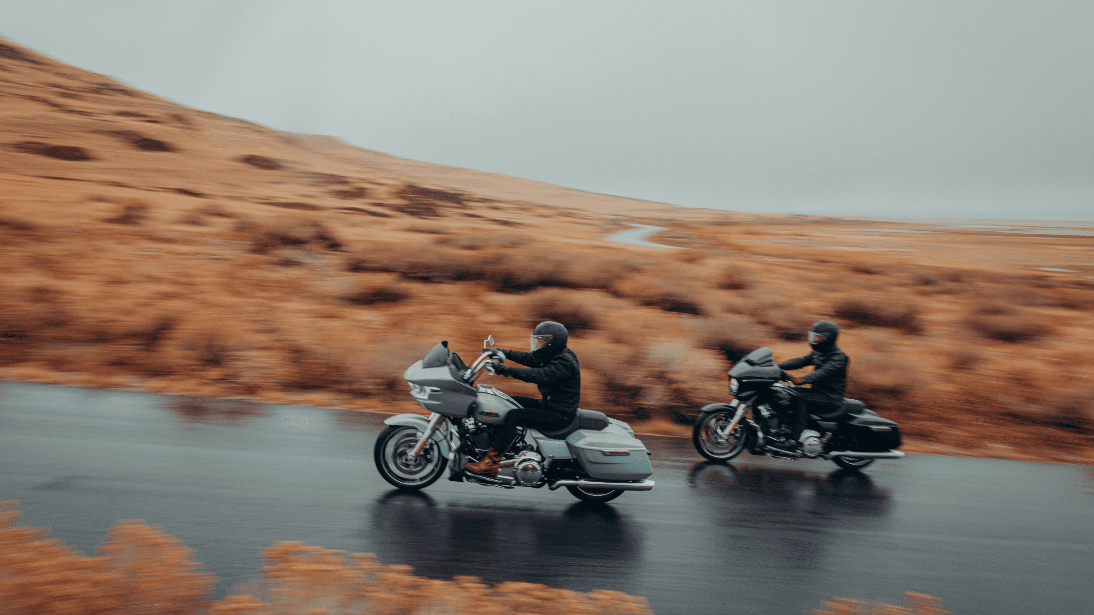 Two touring motorcyclists riding on a winding road in rainy weather.