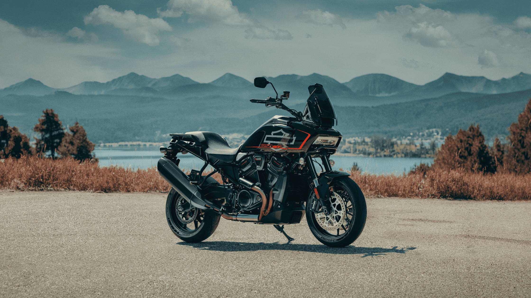 Black adventure motorcycle parked by a scenic lake with mountains.