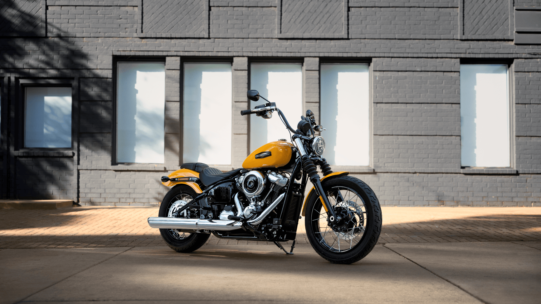 Yellow cruiser motorcycle parked against a modern brick building.