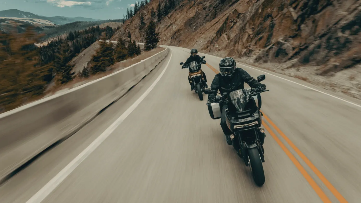 Two adventurers on 2025 Harley-Davidson motorcycles cruise a winding mountain road, surrounded by stunning scenery in Stuart, FL.