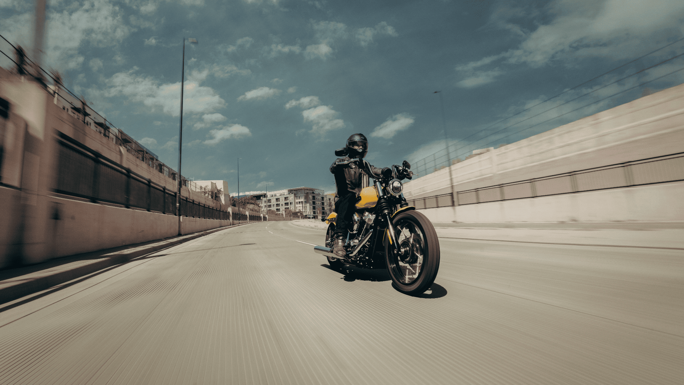 Motorcyclist riding a yellow cruiser on an open city highway.