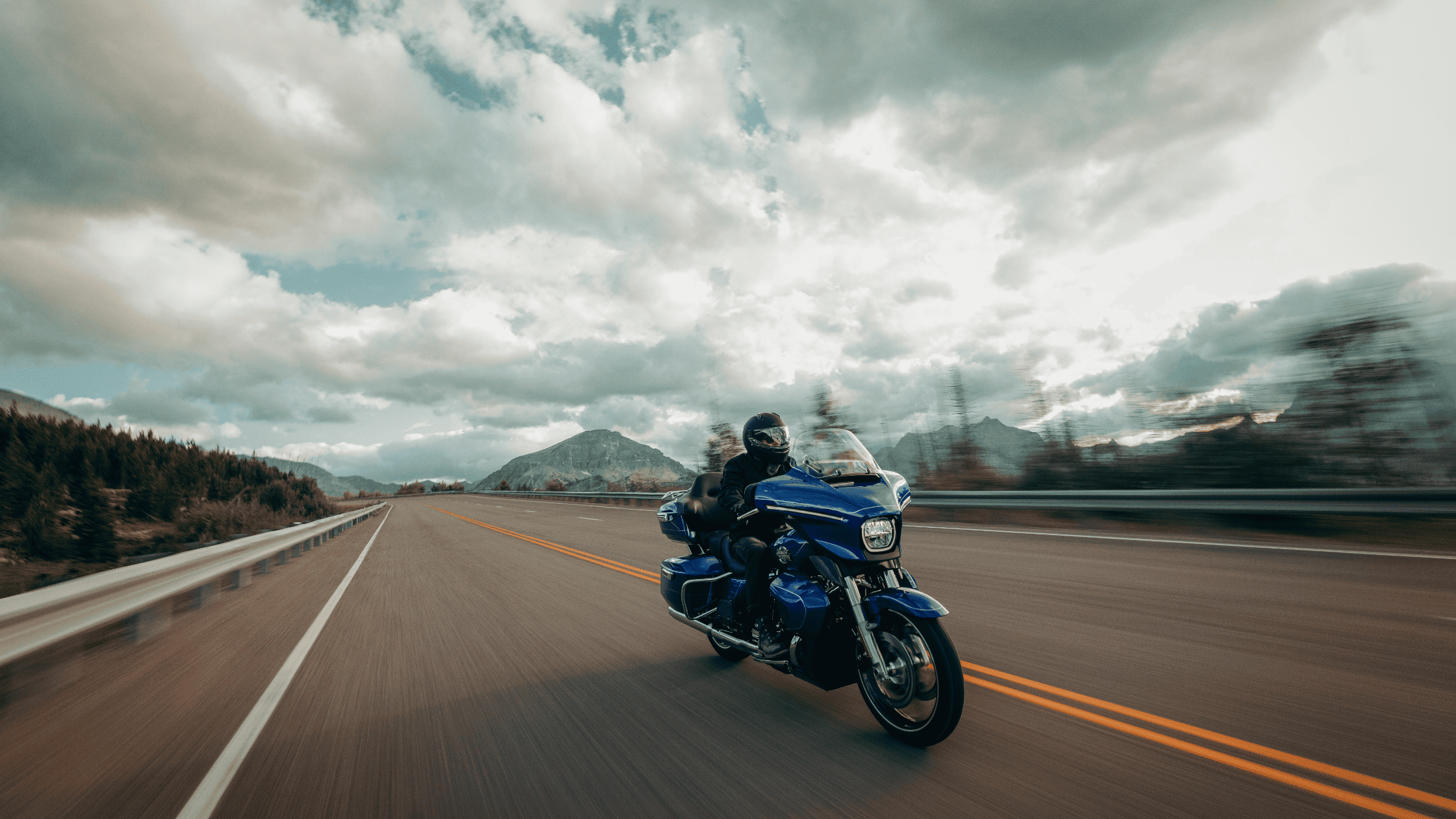 Rider cruising on a blue touring motorcycle along a scenic highway.