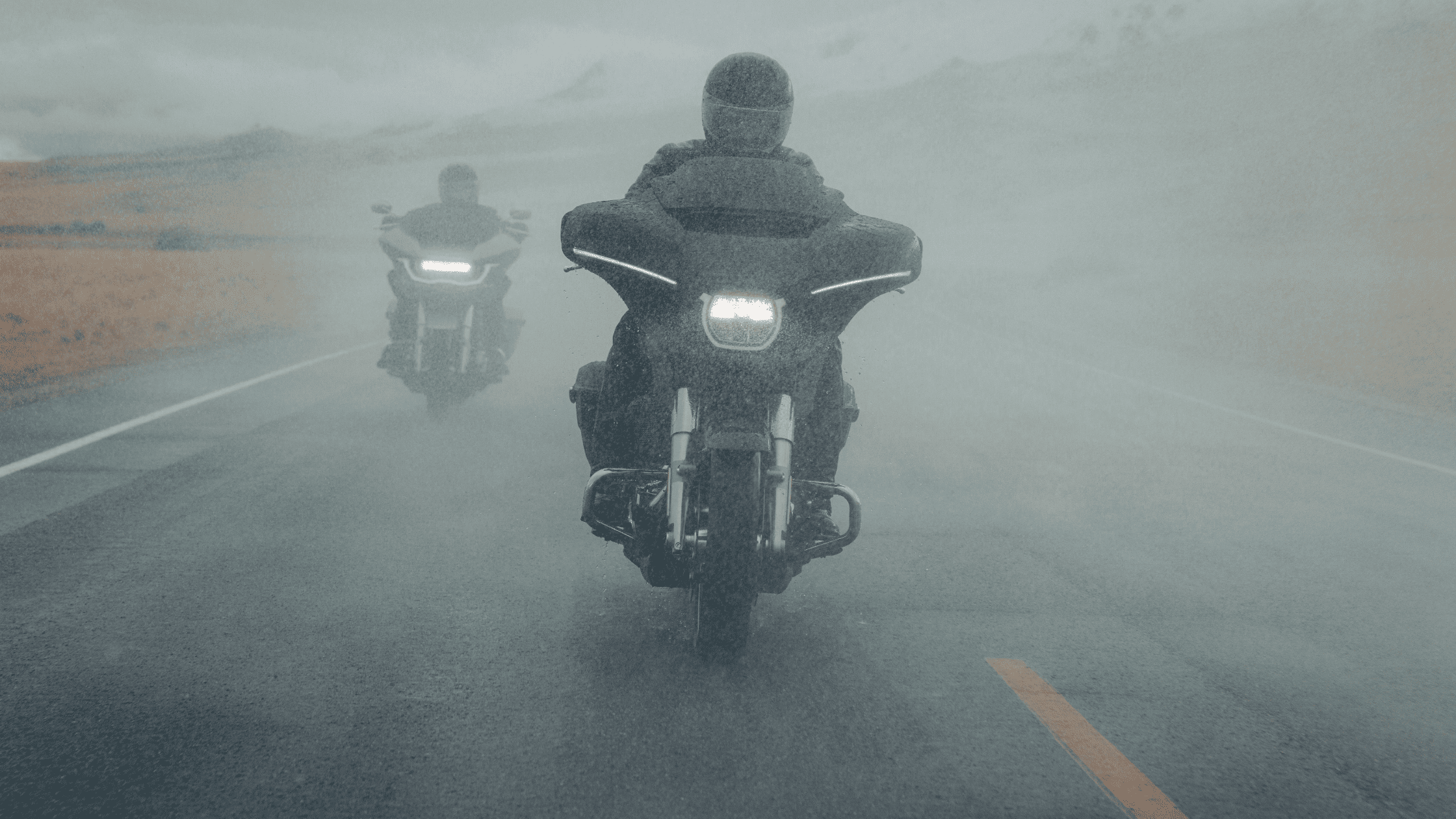 Two touring motorcyclists riding through heavy rain on the highway.