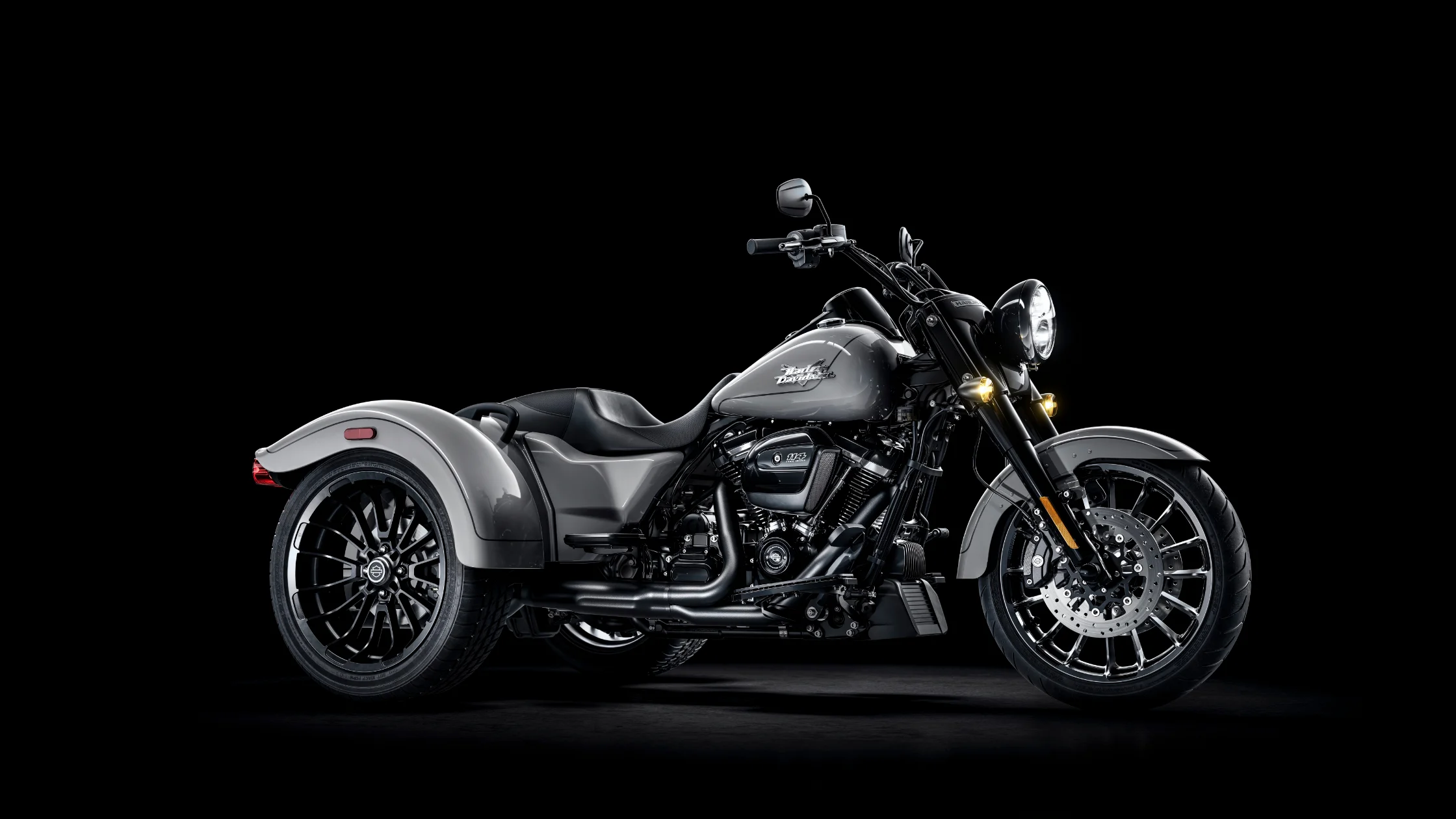 2025 Harley-Davidson Freewheeler in sleek gray, set against a dramatic black background, showcasing its bold styling, blacked-out finishes, and confident three-wheel stance.