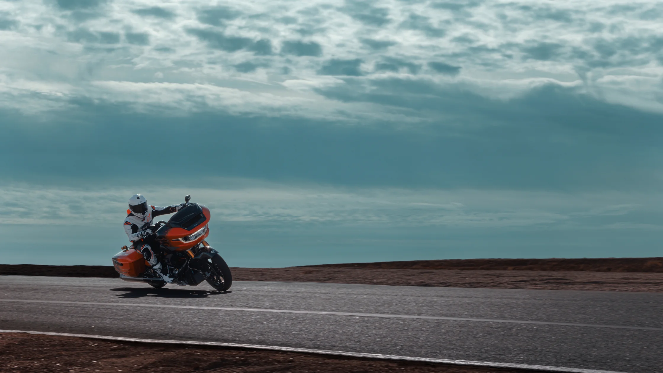 A rider in full racing gear leans aggressively into a turn on the 2025 Harley-Davidson® CVO Road Glide RR, showcasing its precision handling and aerodynamic design.