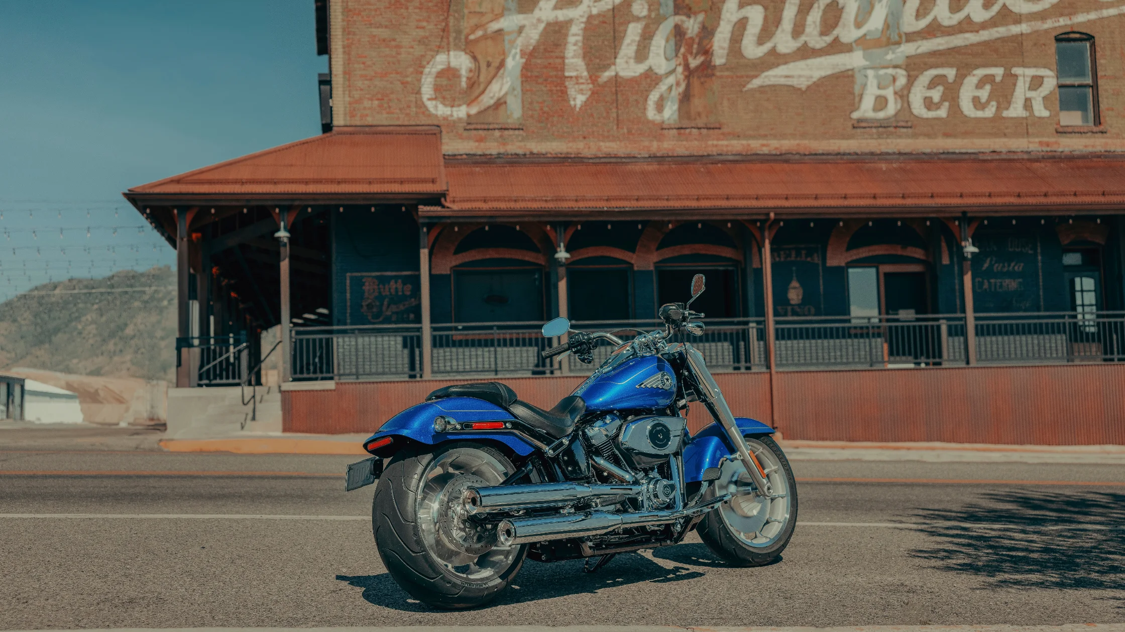 2025 Fat Boy® shines in chrome near vintage Highlands Beer sign on a rustic city street.