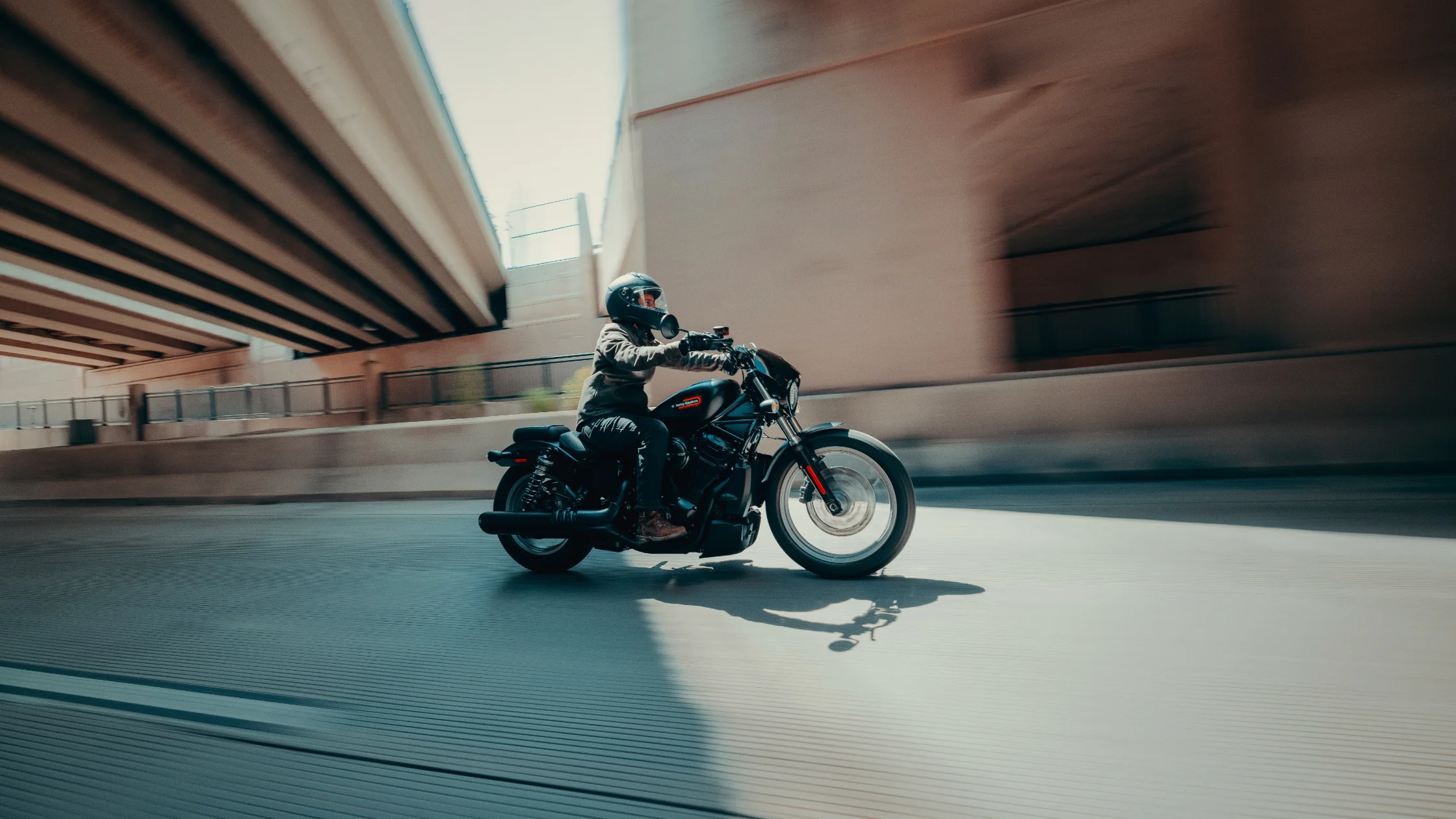 2025 Nightster® S moves under urban overpass with rider in motion through city shadows.