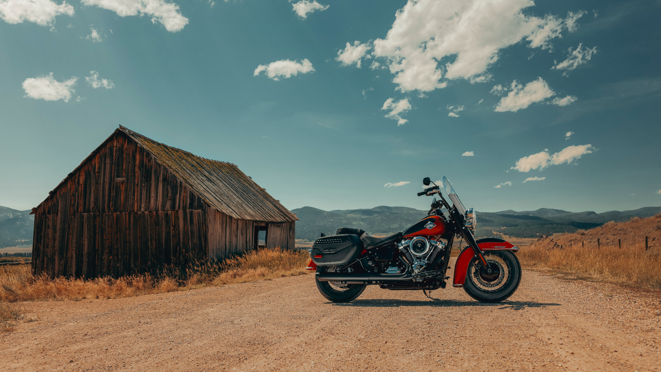 Red 2025 Harley-Davidson® Heritage Classic parked beside a rustic barn on a rural dirt road.