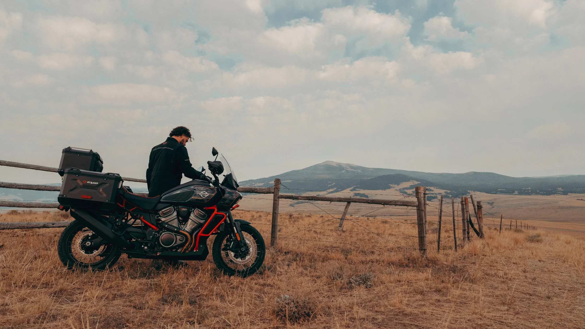 2025 CVO™ Pan America® rider pauses at a scenic ridge with mountain views and dry grassland.