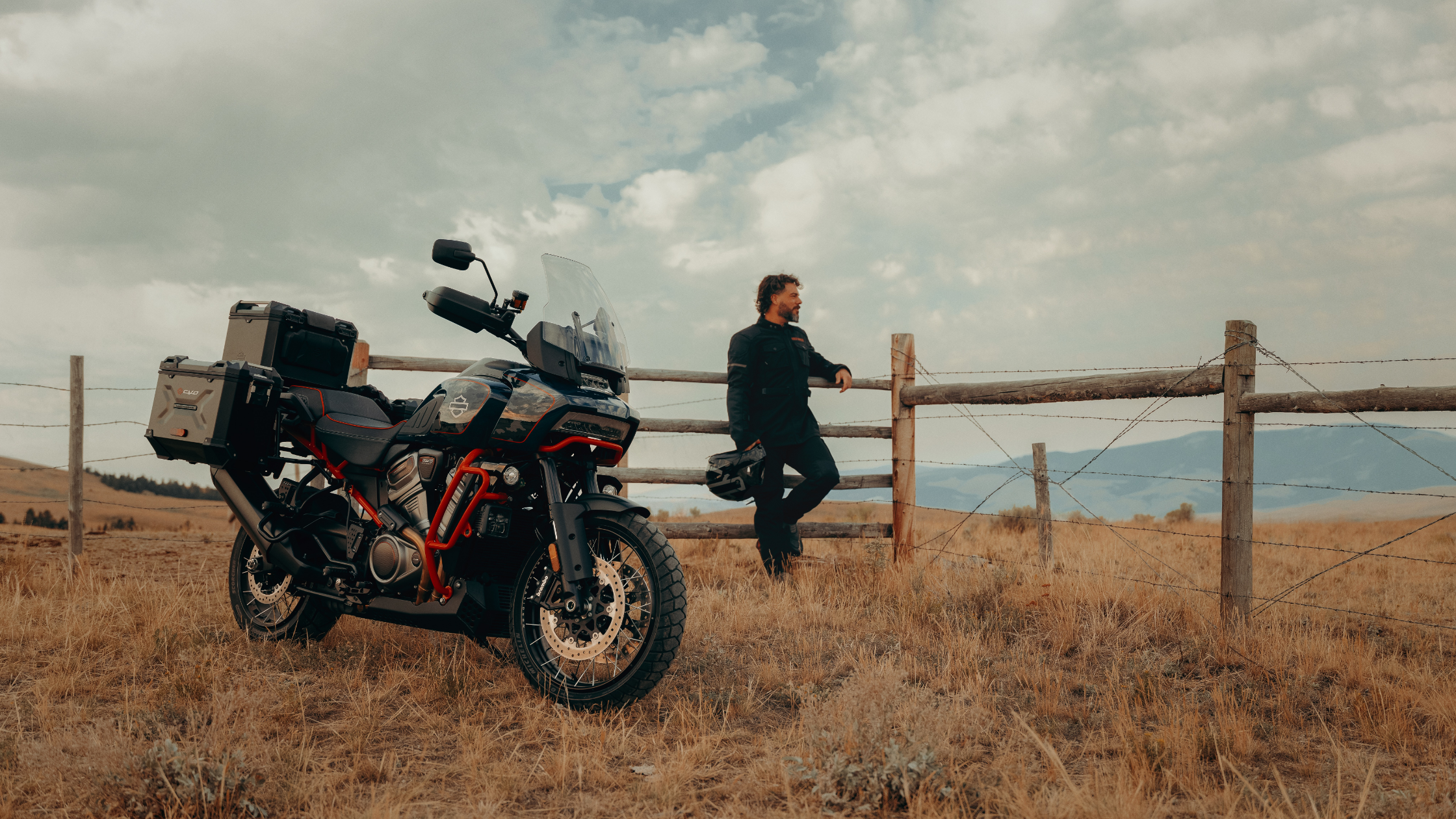 Rider resting near a 2025 Harley-Davidson® CVO™ Pan America® parked in a rural field by a fence.