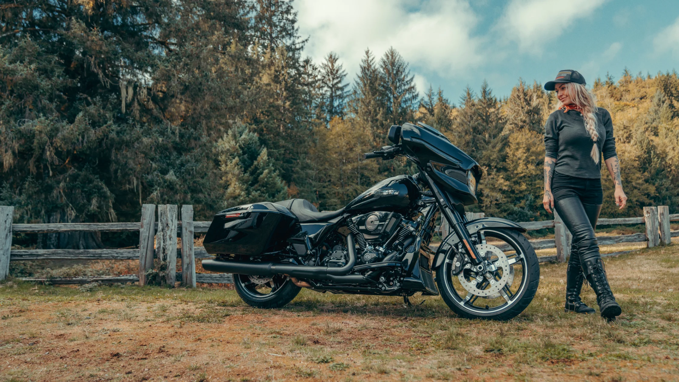 Woman walking by 2025 Harley-Davidson® Street Glide® parked in front of rustic forest fence.