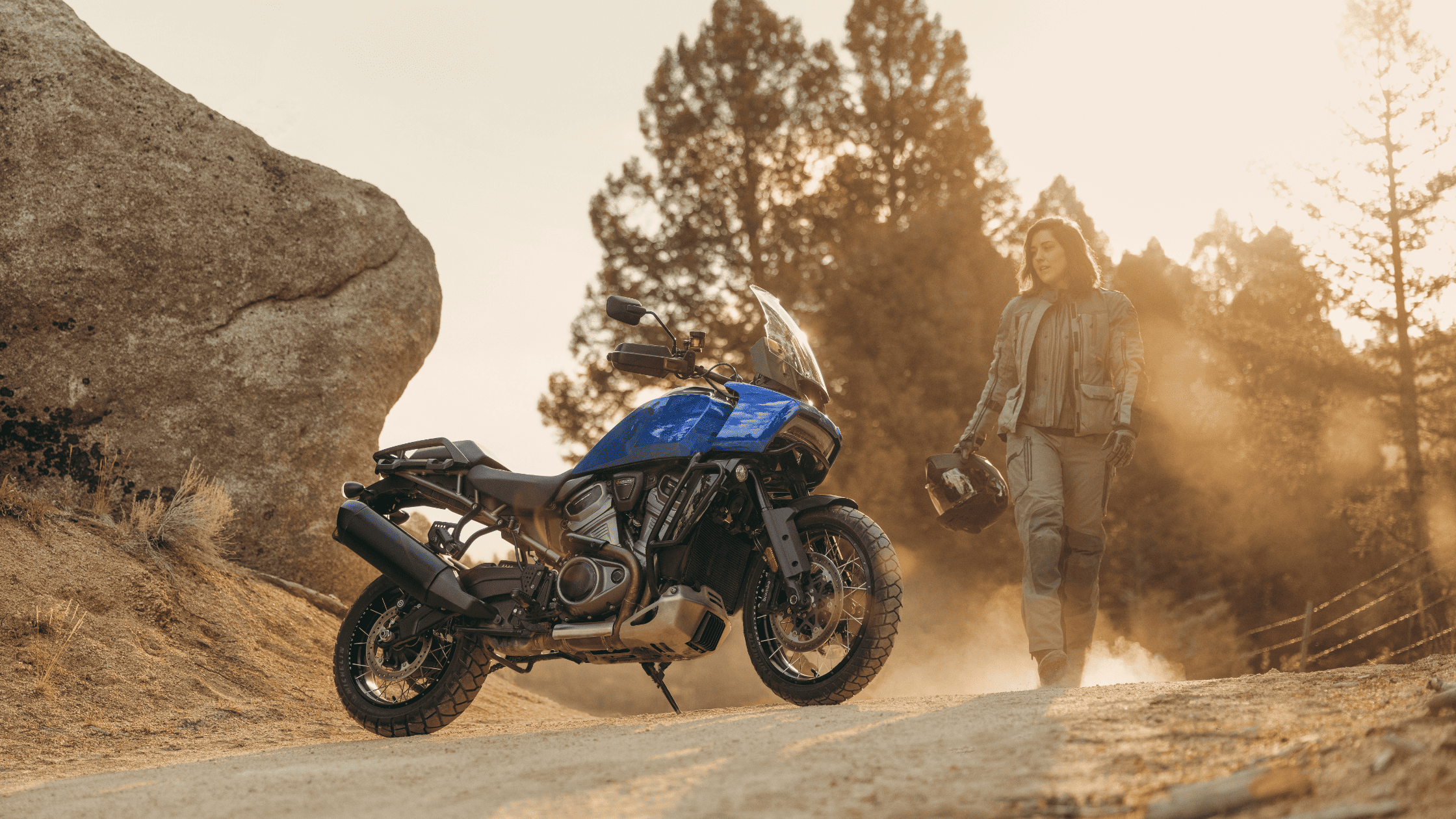Rider walking toward a 2025 Harley-Davidson® Pan America™ 1250 Special parked on a dirt trail at sunset