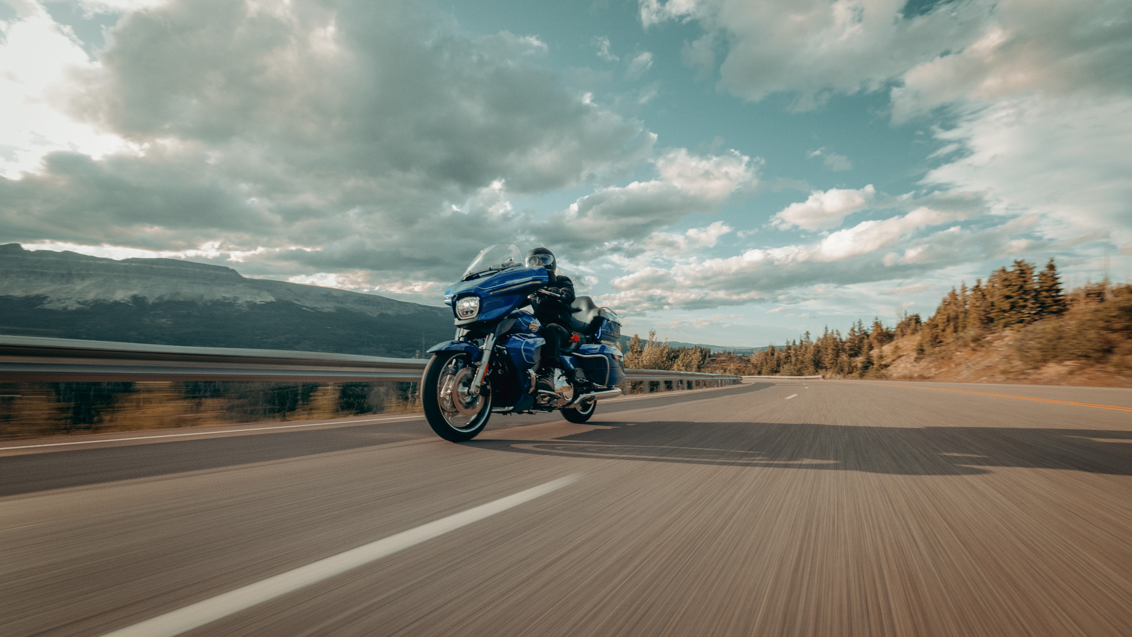 Rider on a 2025 Harley-Davidson® Street Glide® Ultra cruising on an open highway with mountain views