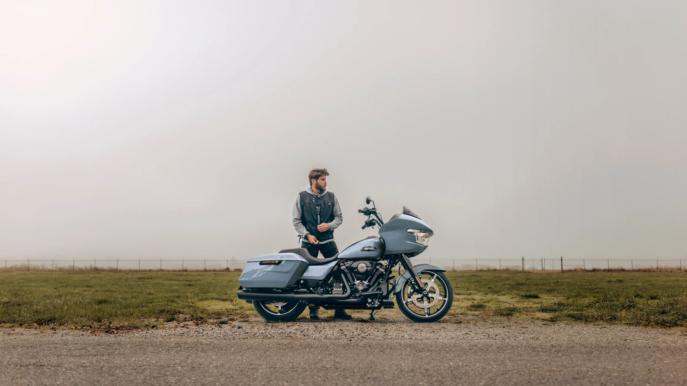 Man standing beside 2025 Harley-Davidson® Road Glide® in matte gray on a foggy open road