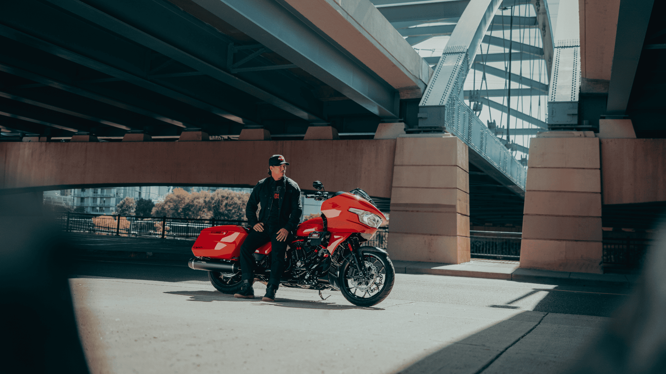 Rider sitting on a 2025 Harley-Davidson® CVO™ Road Glide® ST in red under a modern city bridge