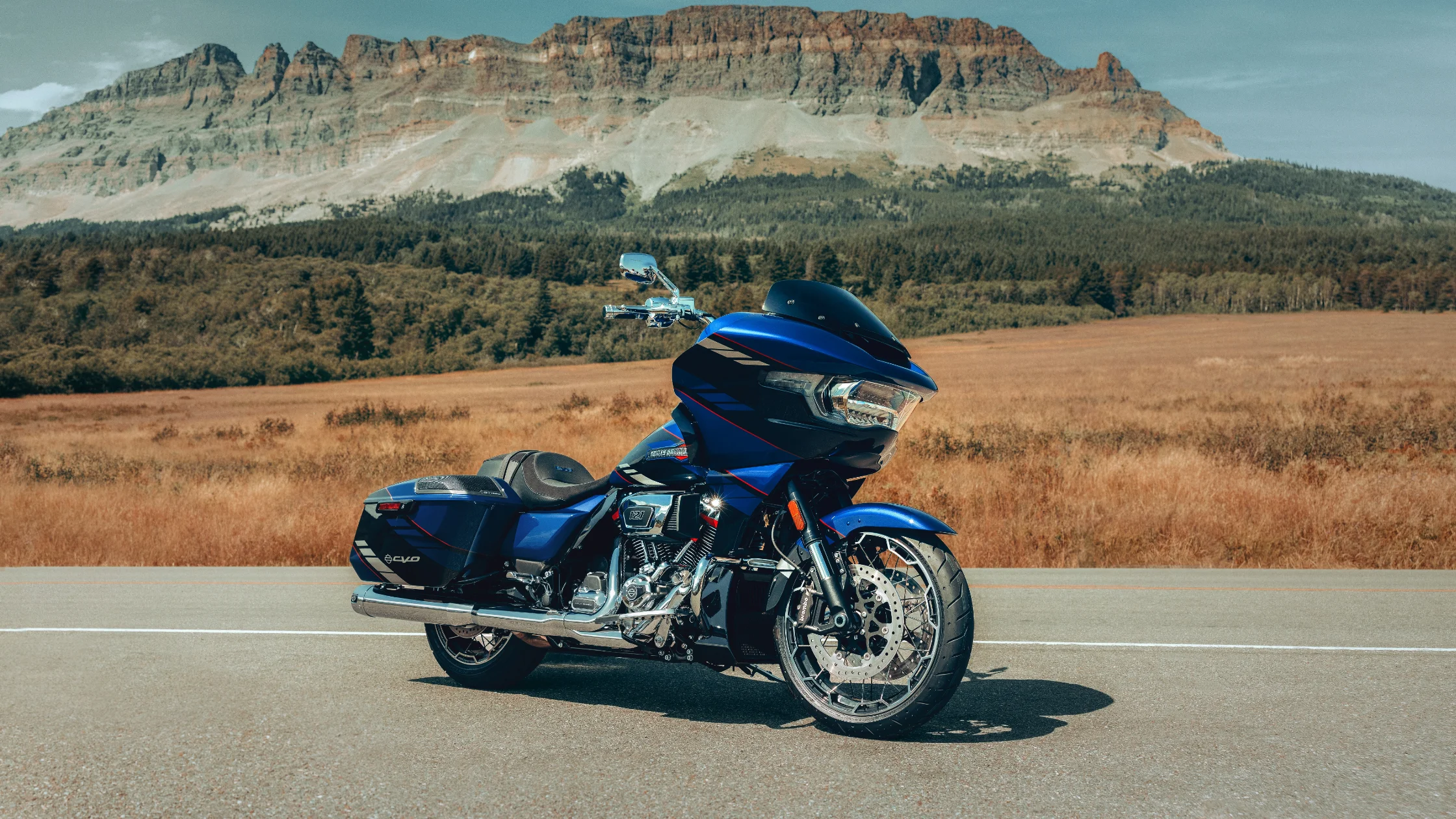 2025 Harley-Davidson® CVO™ Road Glide® motorcycle in blue parked on an open road with scenic mountain backdrop.
