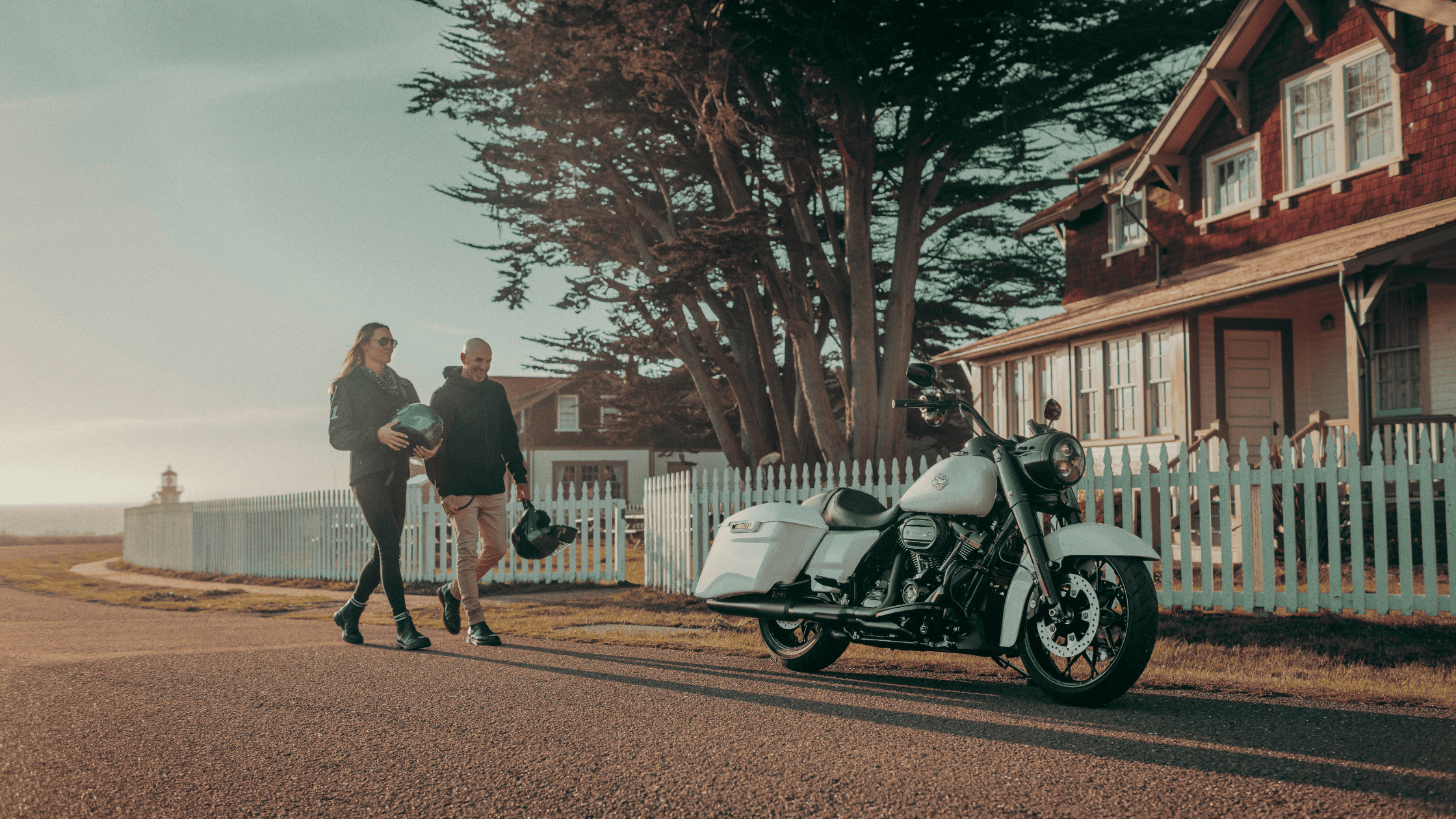 Couple walking toward a 2025 Harley-Davidson Road King Special parked near coastal homes and trees.