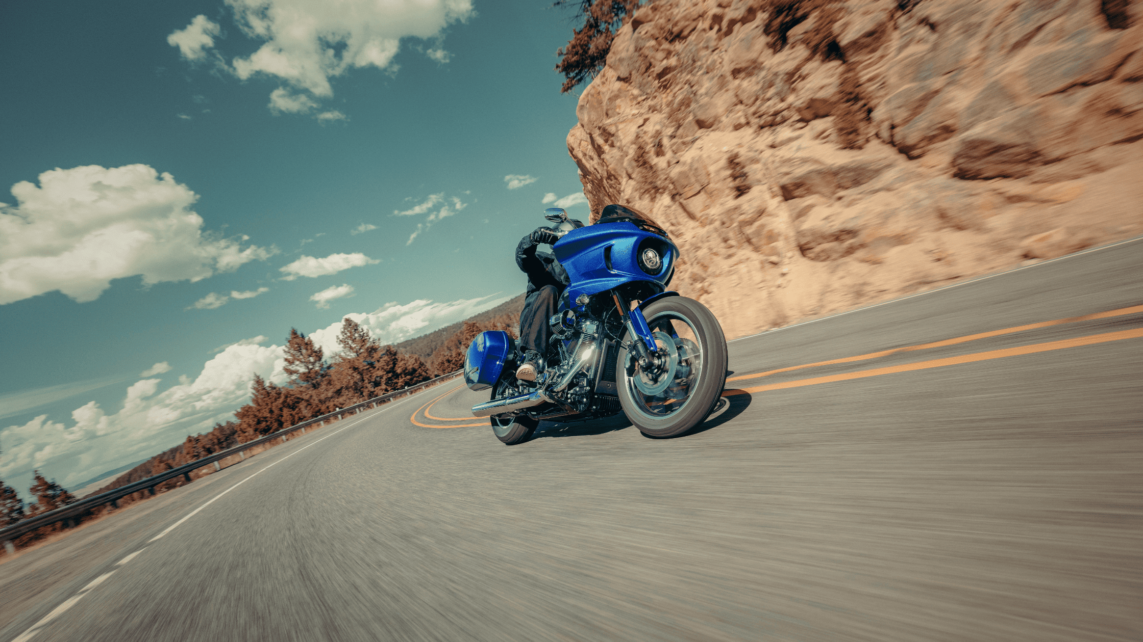 2025 Harley-Davidson Low Rider ST leans into a mountain curve under a blue sky.