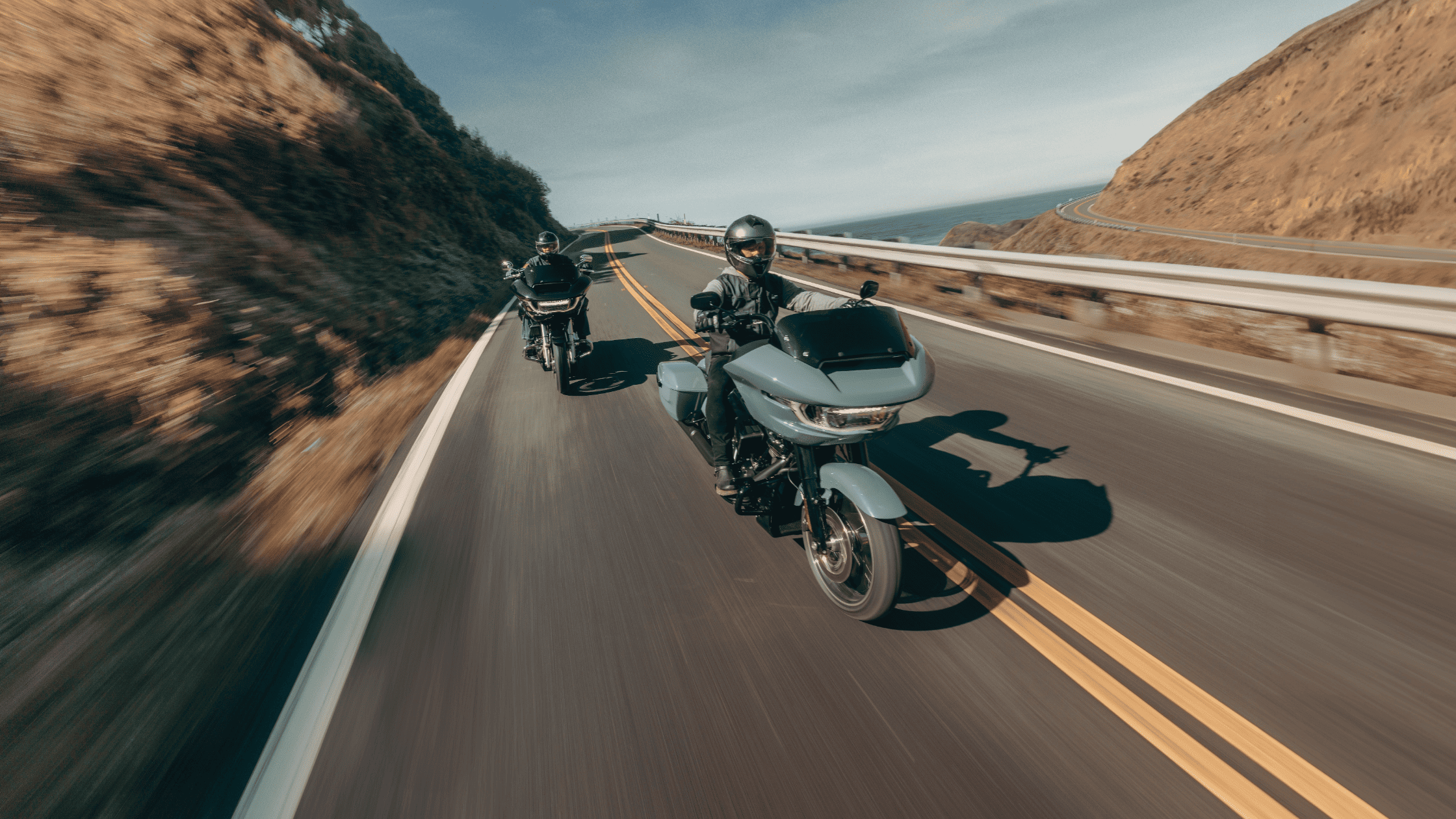 Two riders on 2025 Harley-Davidson® Road Glide® Skyline™ OS motorcycles ride along a coastal bend near Bentonville, built for confident women who love the open road.