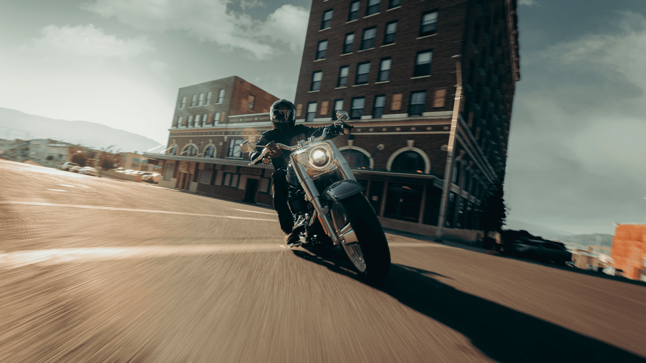 2025 Harley-Davidson Fat Boy leans into a city intersection in front of a tall brick hotel.