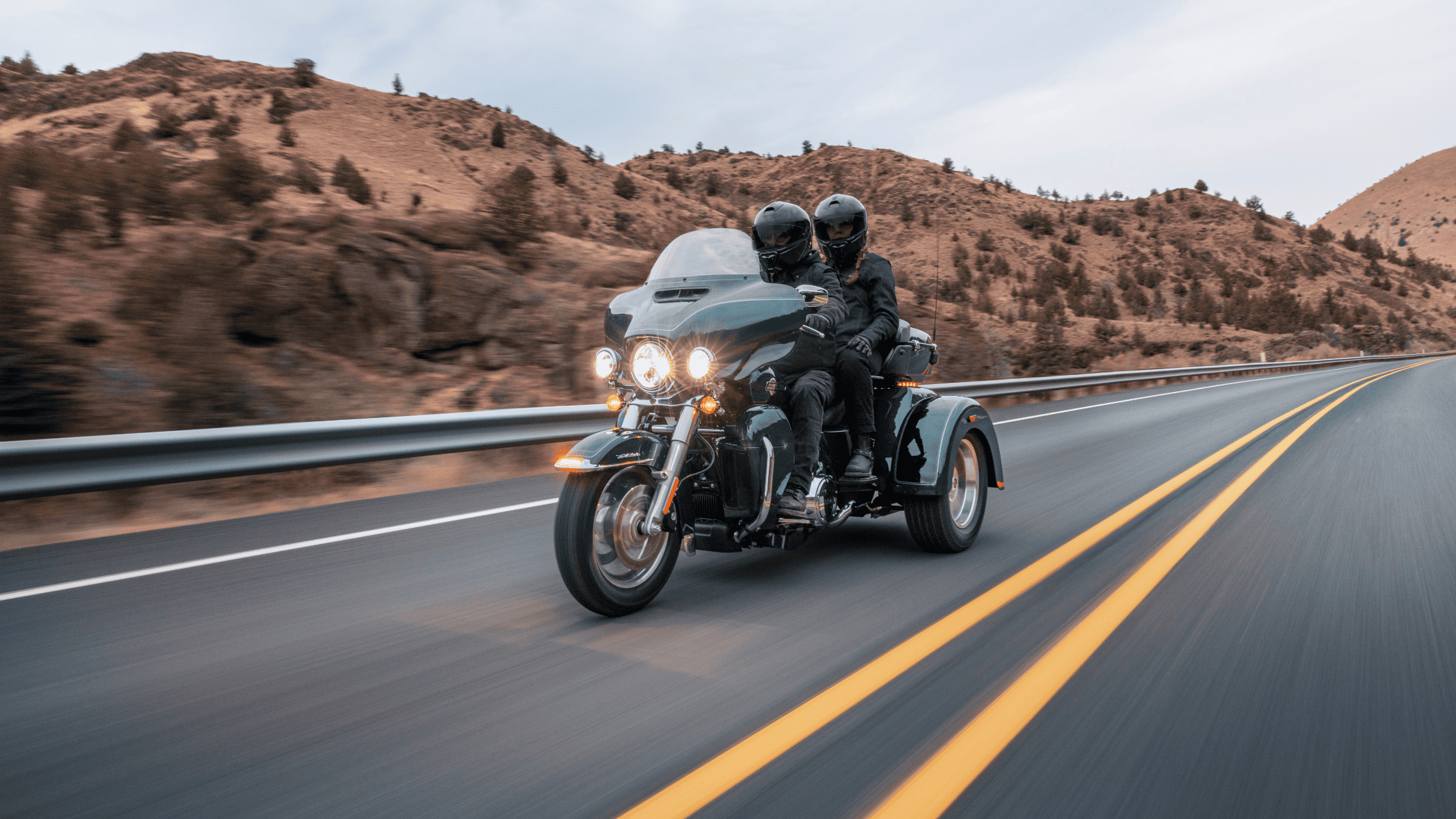 Two-up riders on a 2025 Harley-Davidson Tri Glide Ultra cruising scenic mountain roads.
