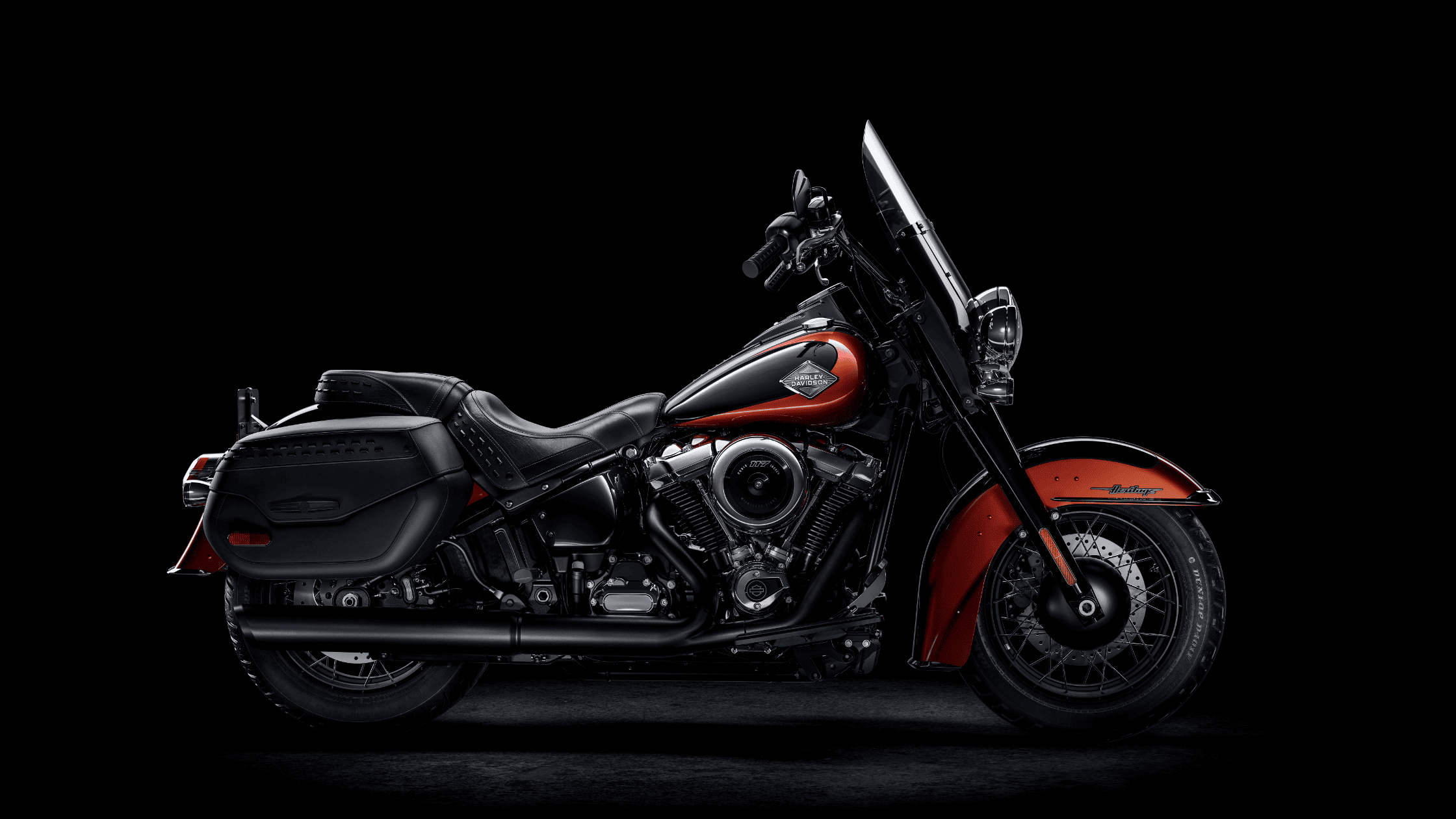 Side view of a 2025 Harley-Davidson® Heritage Classic in red and black with saddlebags and windshield, parked under dramatic lighting near West Palm Beach, FL.