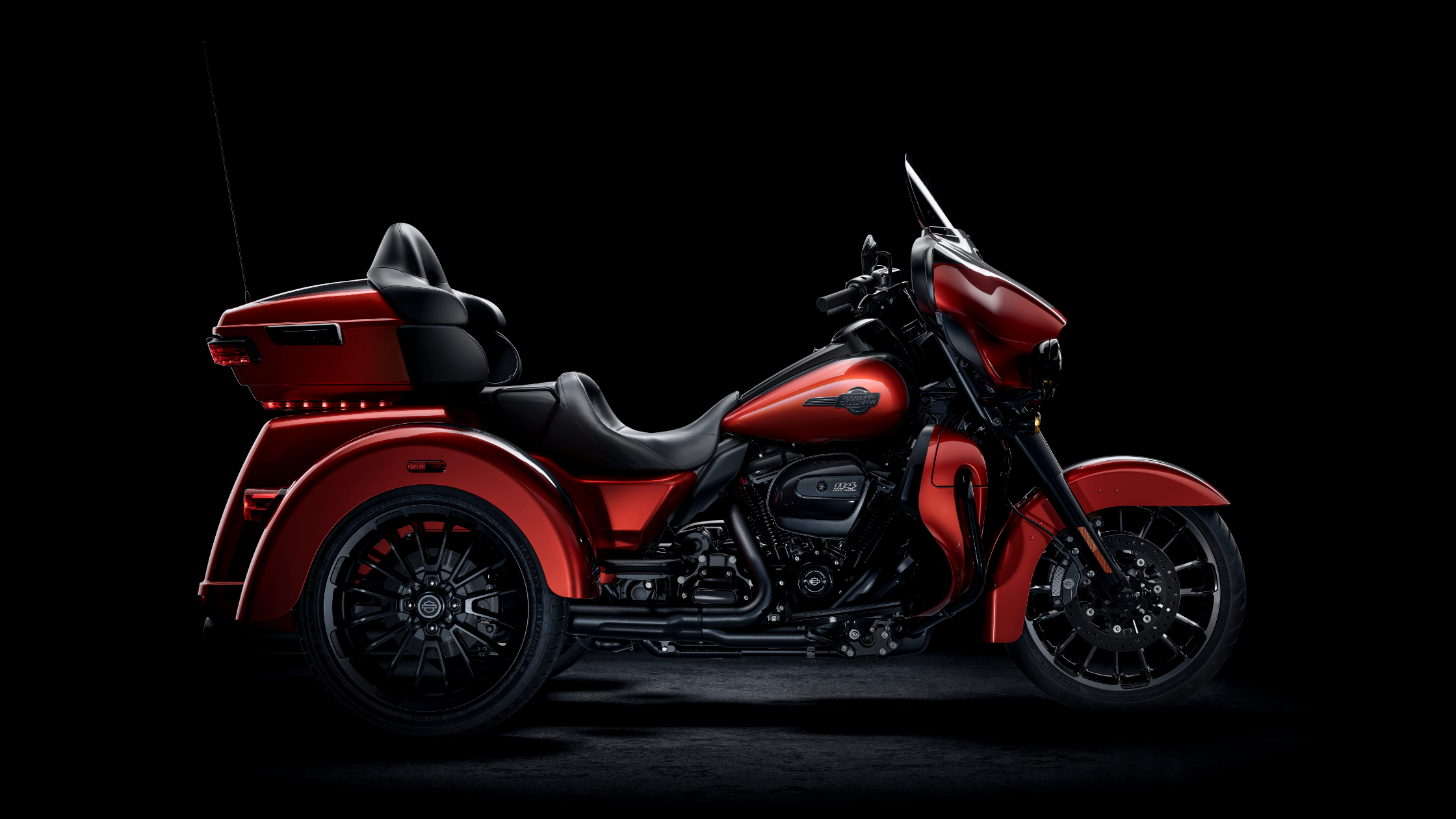 2025 Harley-Davidson Tri Glide Ultra in vivid red with black accents, side profile on a dark studio background.