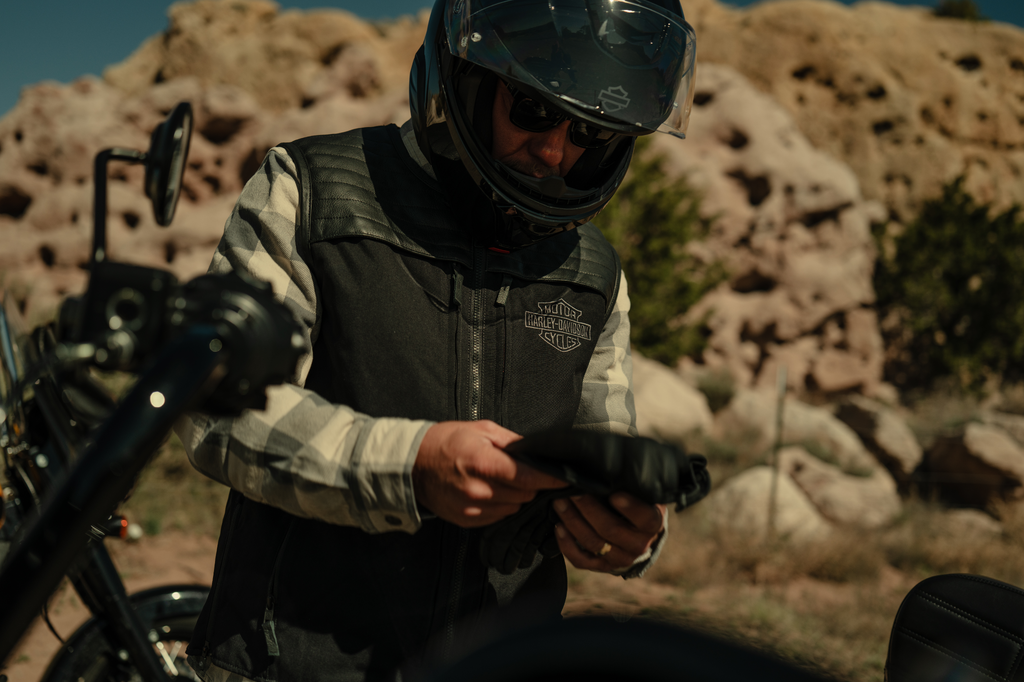 Harley-Davidson rider wearing a full helmet, leather vest, and putting on leather gloves for a ride