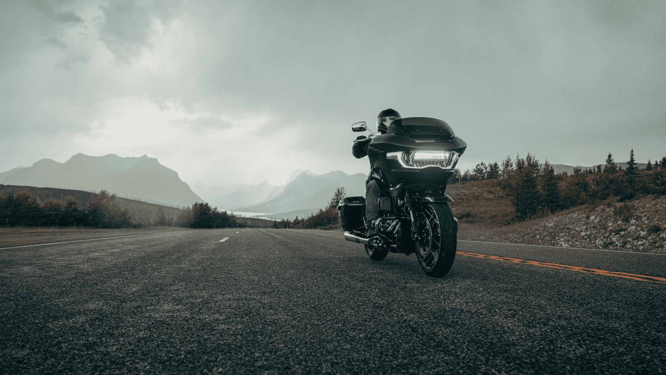 Rider on a 2025 Harley-Davidson CVO Road Glide cruising along a scenic highway with distant mountains under cloudy skies.