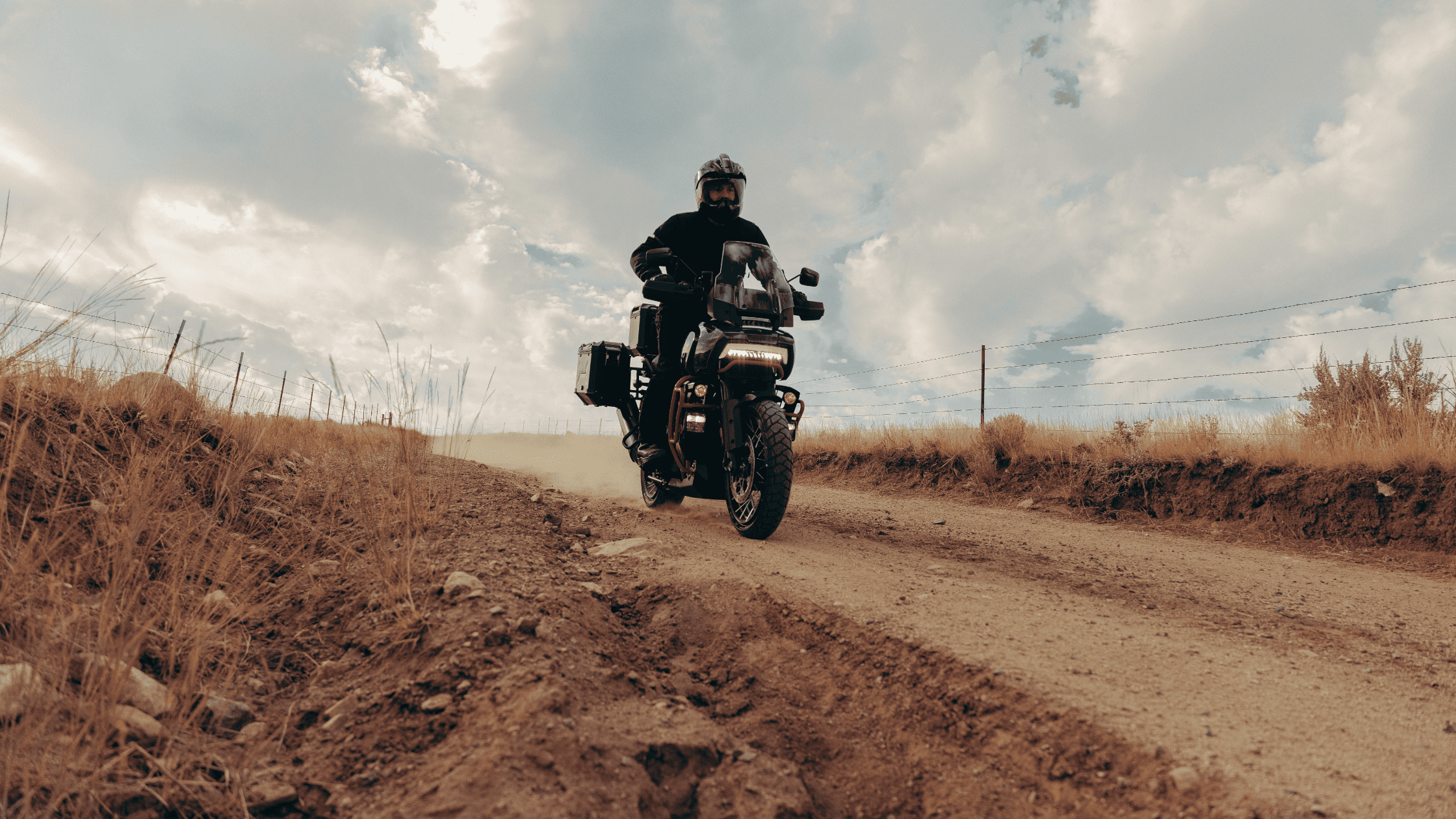 Rider on a black 2025 Harley-Davidson® CVO™ Pan America® navigating a dusty dirt trail under a cloudy sky