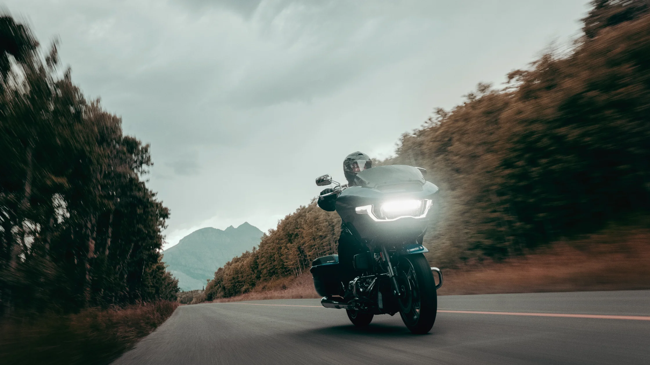 Front view of a rider on a 2025 CVO Road Glide® in motion, LED headlight glowing on forest road.