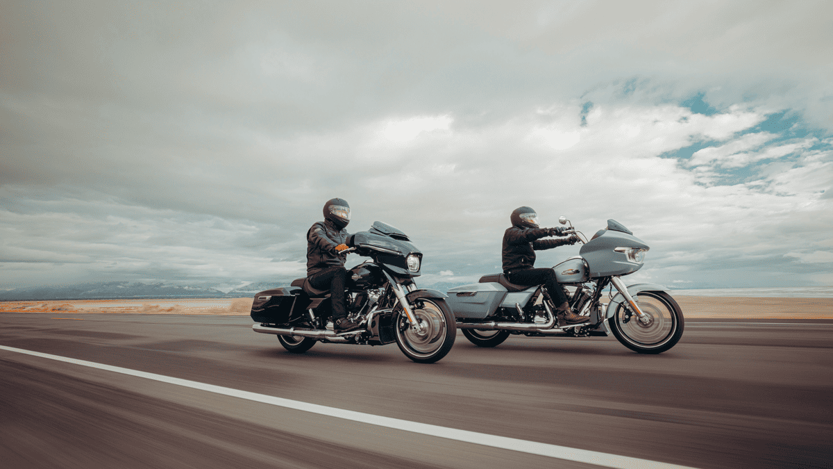 Two 2025 H-D® Grand American Touring motorcycles riding side by side on an open road, featuring Street Glide® and Road Glide® models in motion.