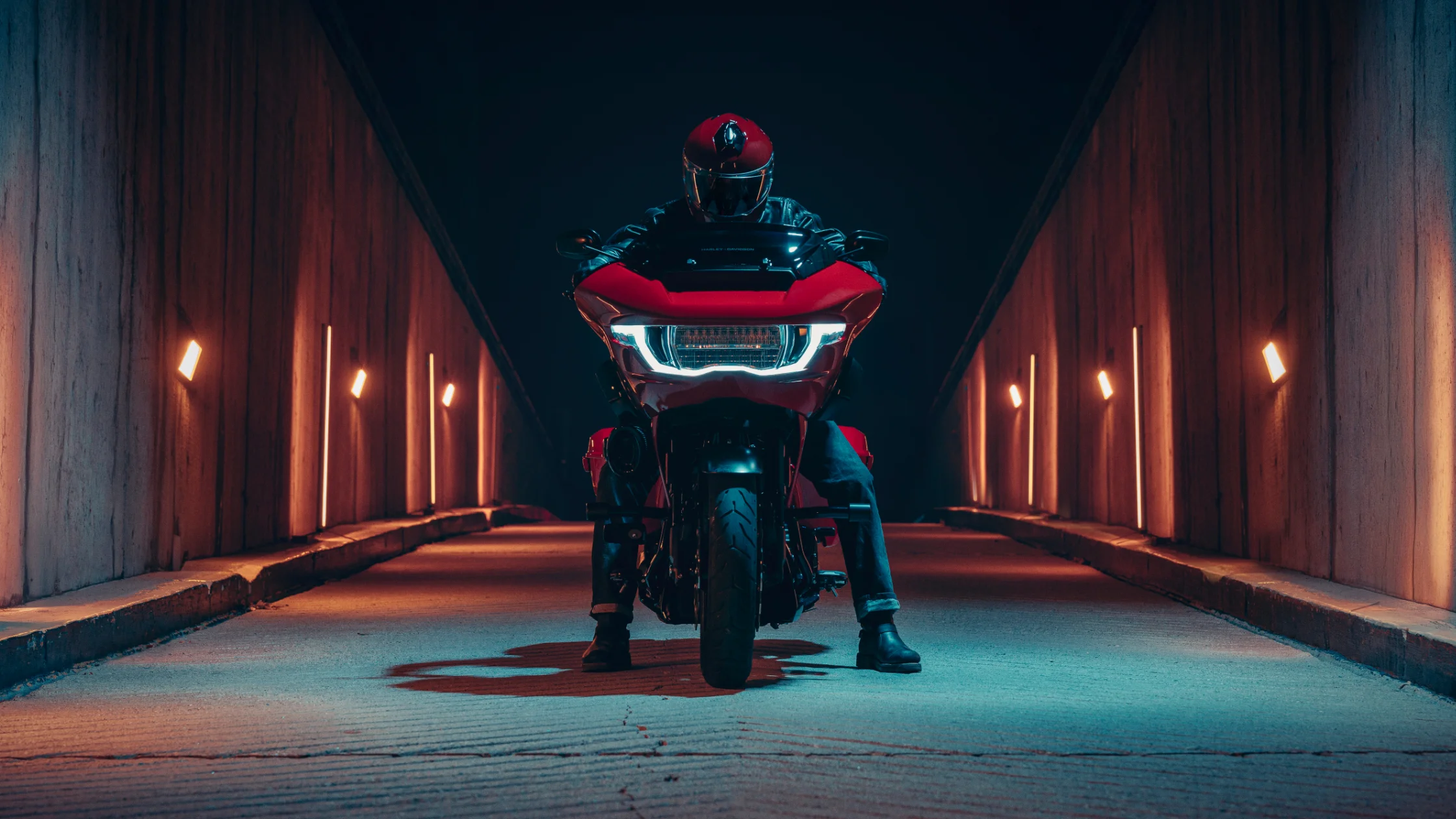 Frontal view of red 2025 H-D® CVO™ Road Glide® ST in tunnel, LED headlight lit, rider in full gear.