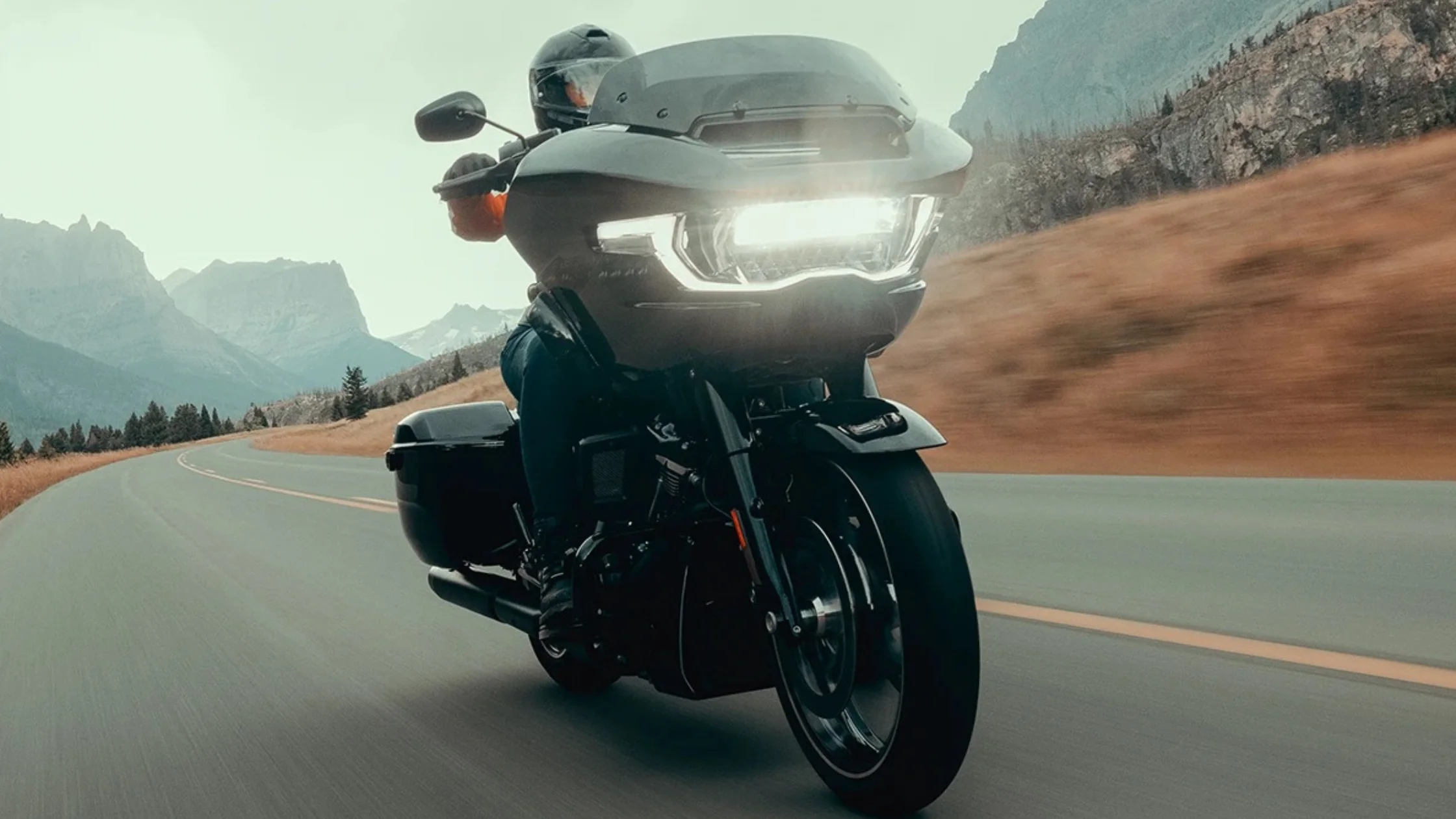Close-up front angle of 2025 H-D® Road Glide® Carryover in motion, LED light blazing on mountain road.