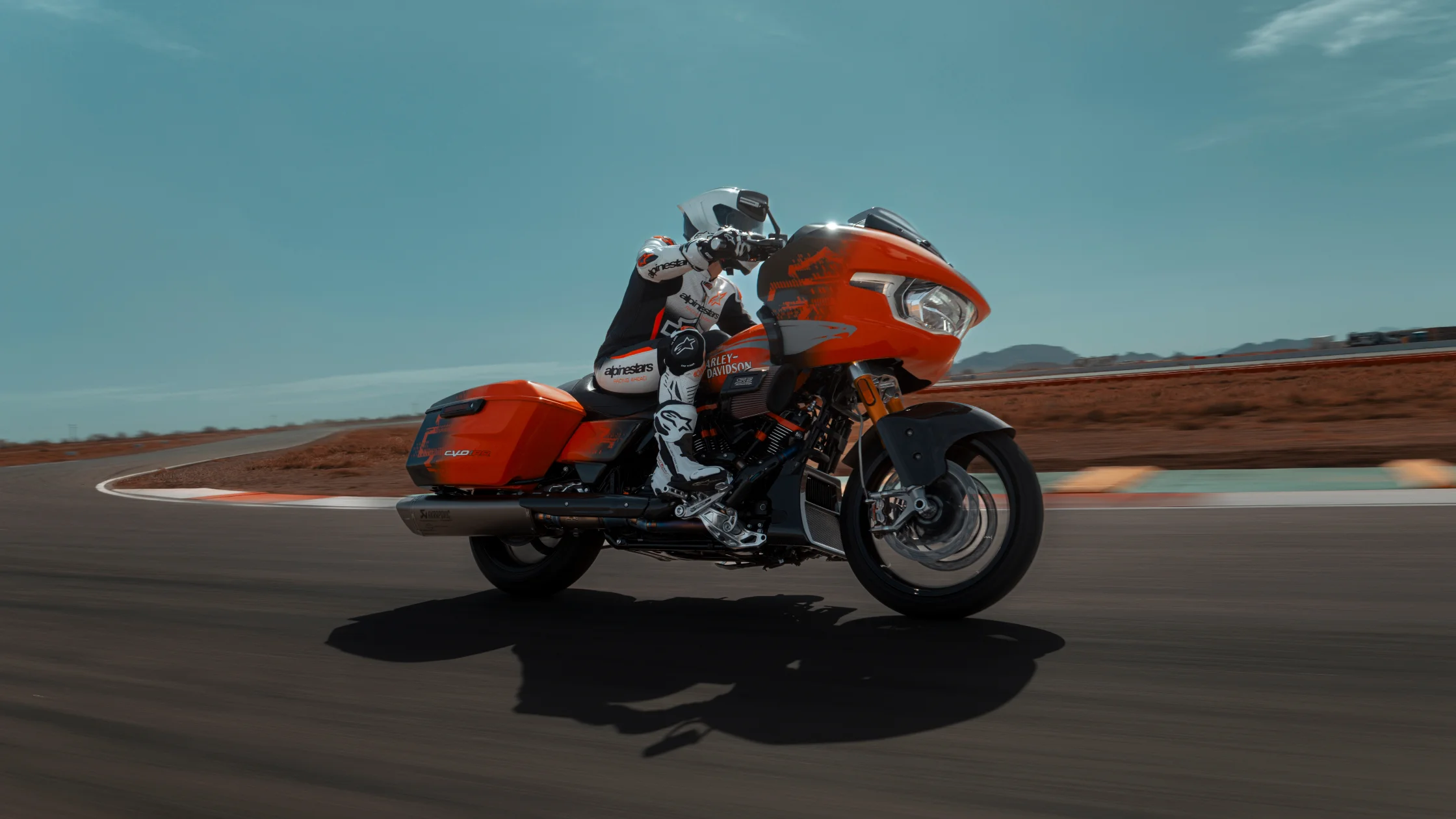 2025 H-D® CVO™ Road Glide® RR in orange on race track, rider in full Alpinestars suit, action shot.