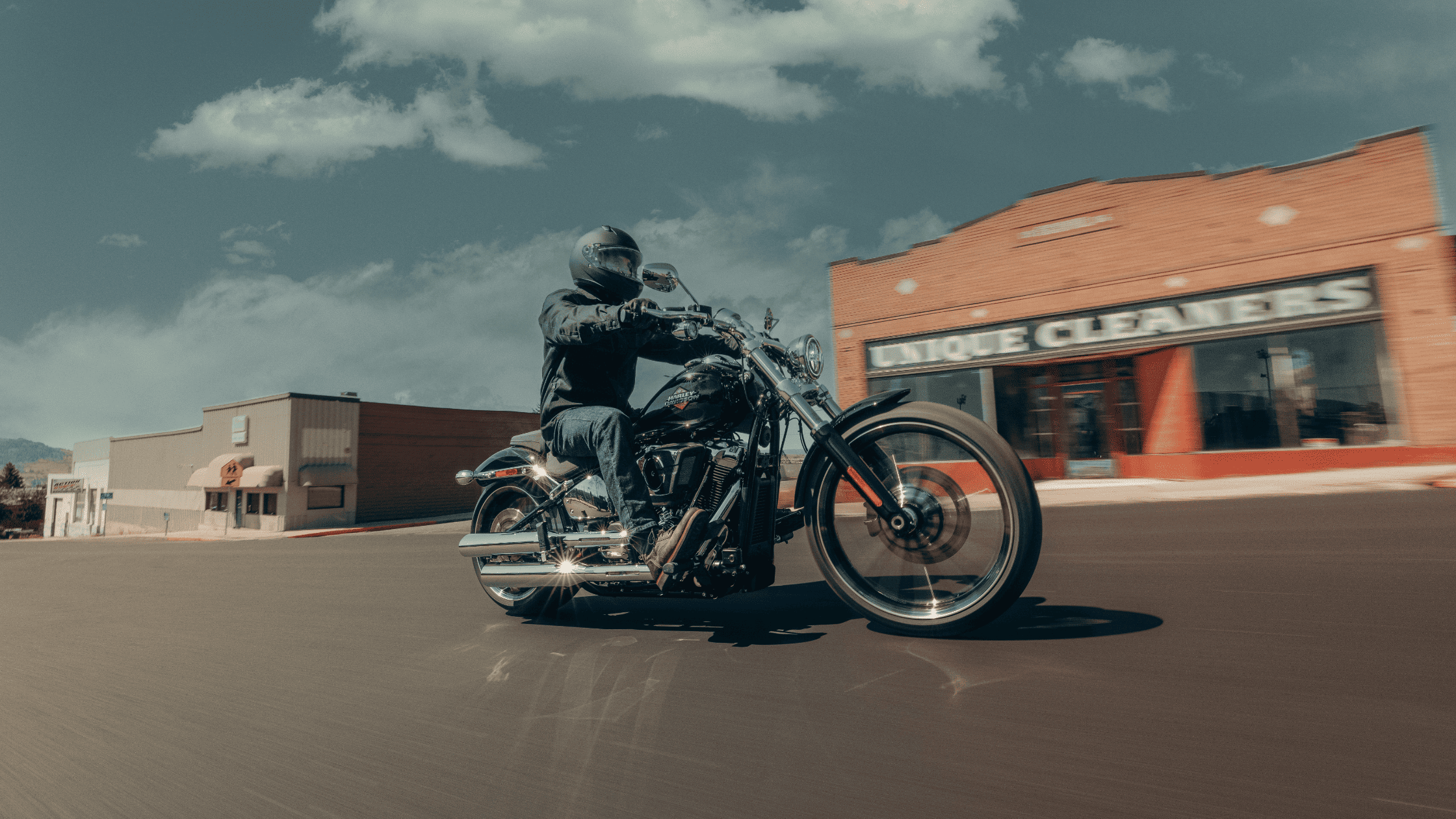 Rider on black 2025 Harley-Davidson Breakout turning past brick shops under sunny sky