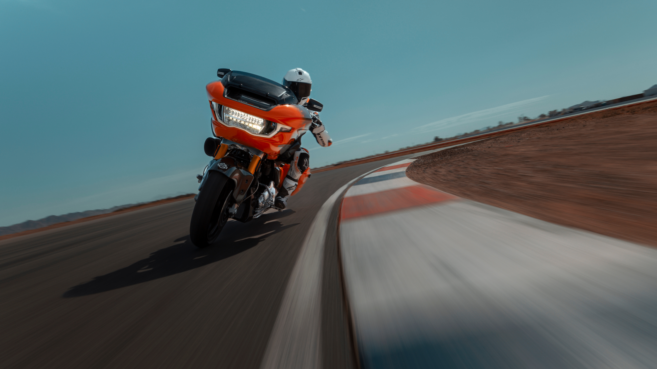 2025 Harley-Davidson® CVO Road Glide RR in orange leaned into racetrack curve.