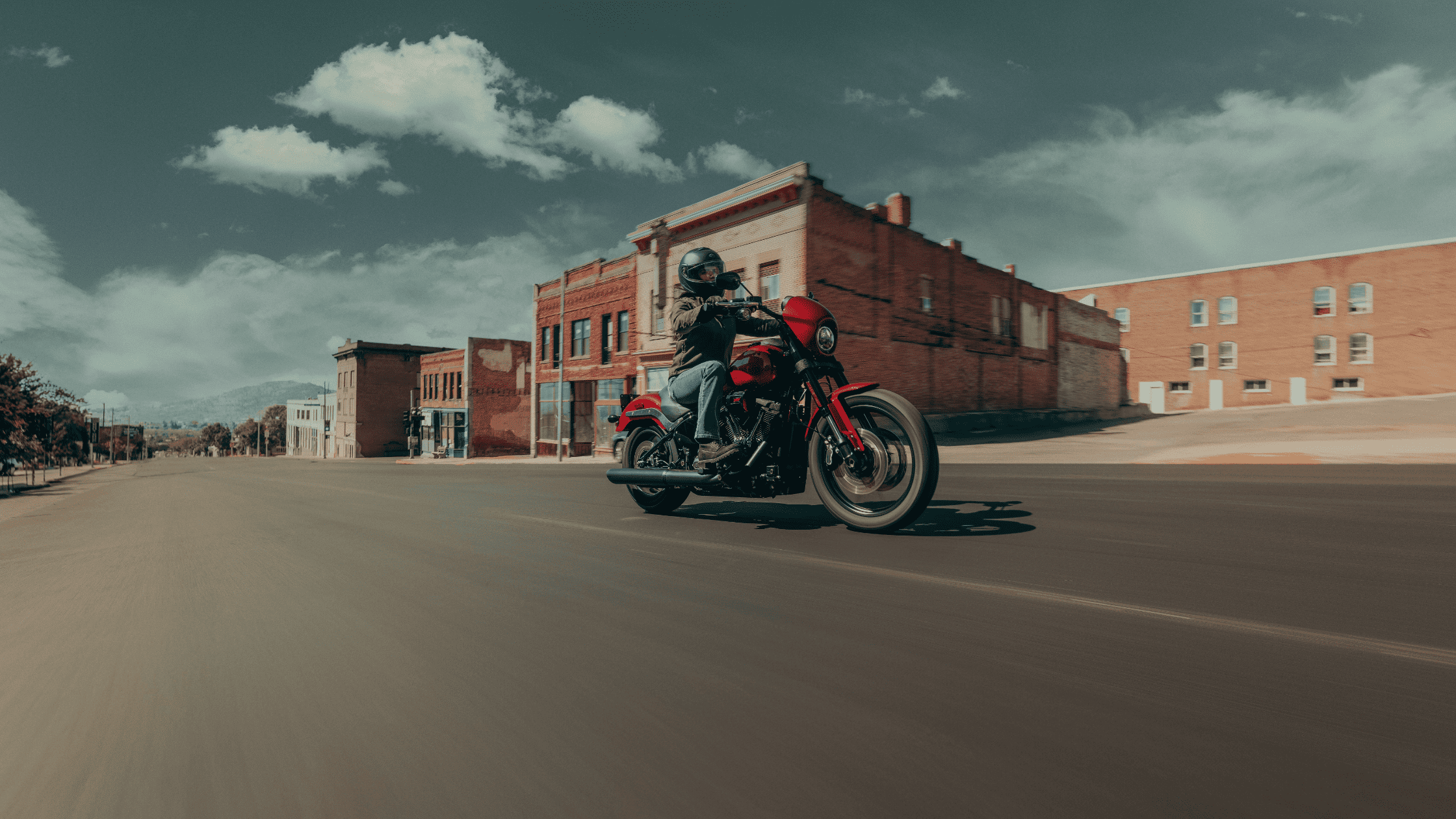 Red Harley-Davidson Low Rider S cruising past brick buildings under blue sky